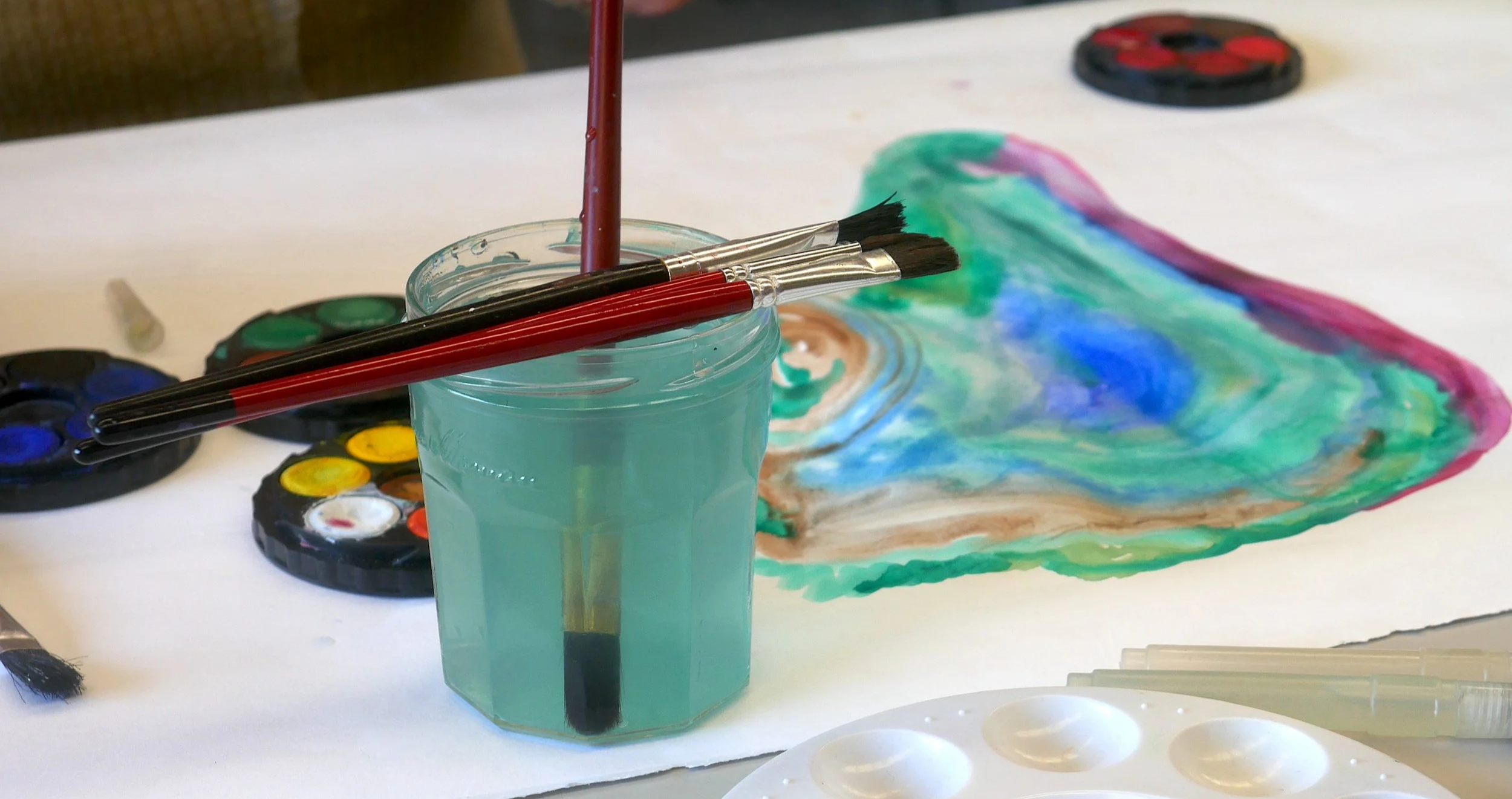 Creative art materials used in art therapy, including paintbrushes and watercolours. Colourful abstract watercolour image.