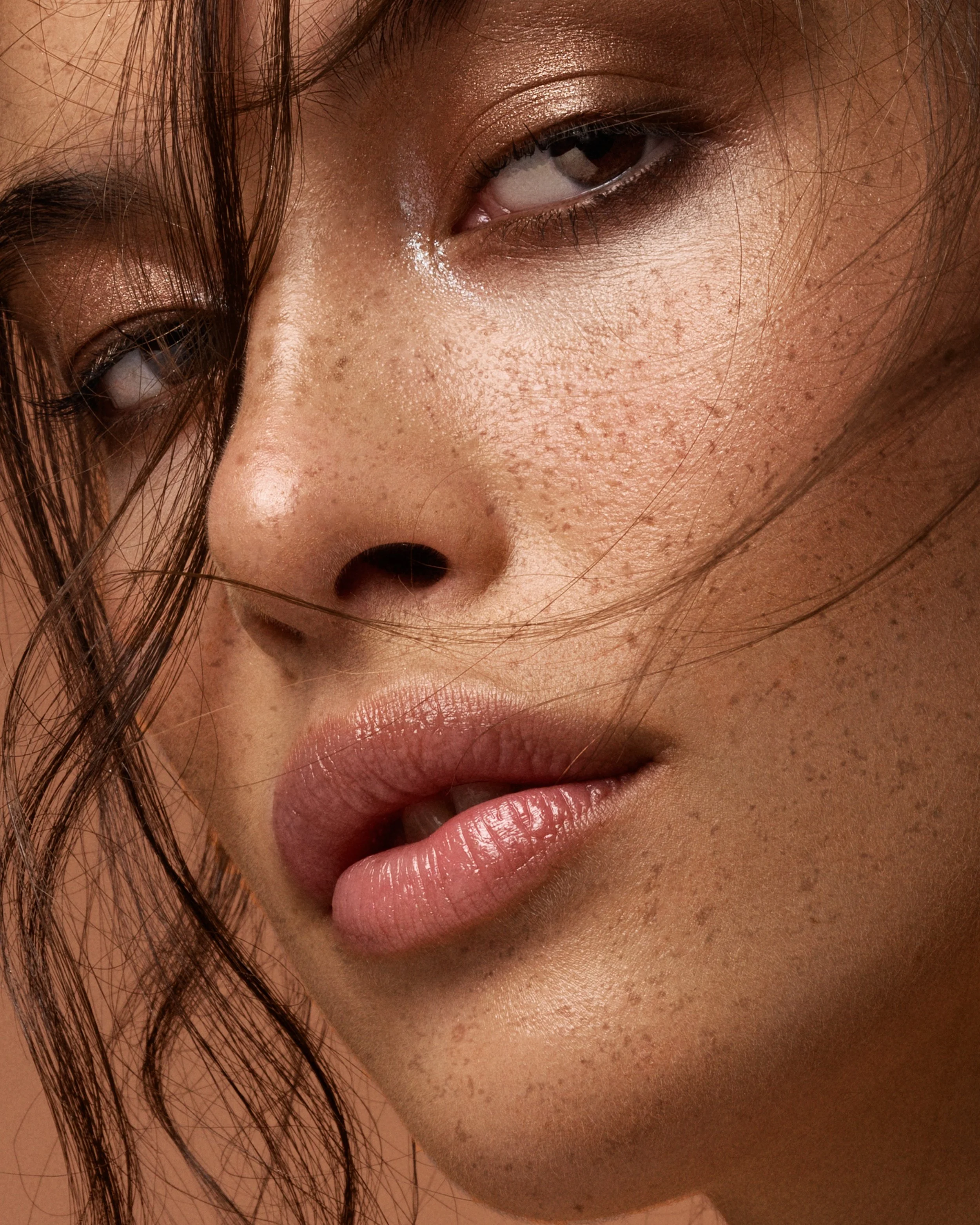 Close-up of a woman's face showing her eye, nose, lips, and freckles with wet skin and hair partially covering her face.
