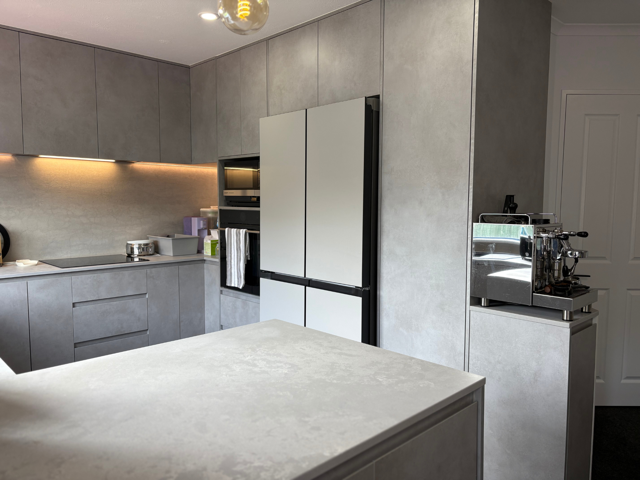 Modern kitchen with gray cabinets, white appliances, and a coffee espresso machine on a countertop.