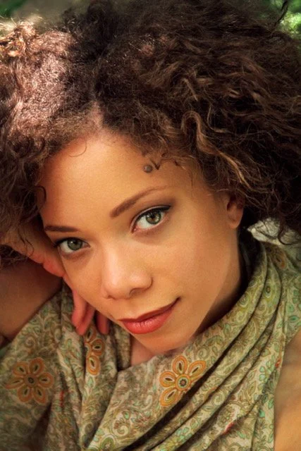 Close-up of a woman with curly hair wearing a patterned scarf, looking into the camera.