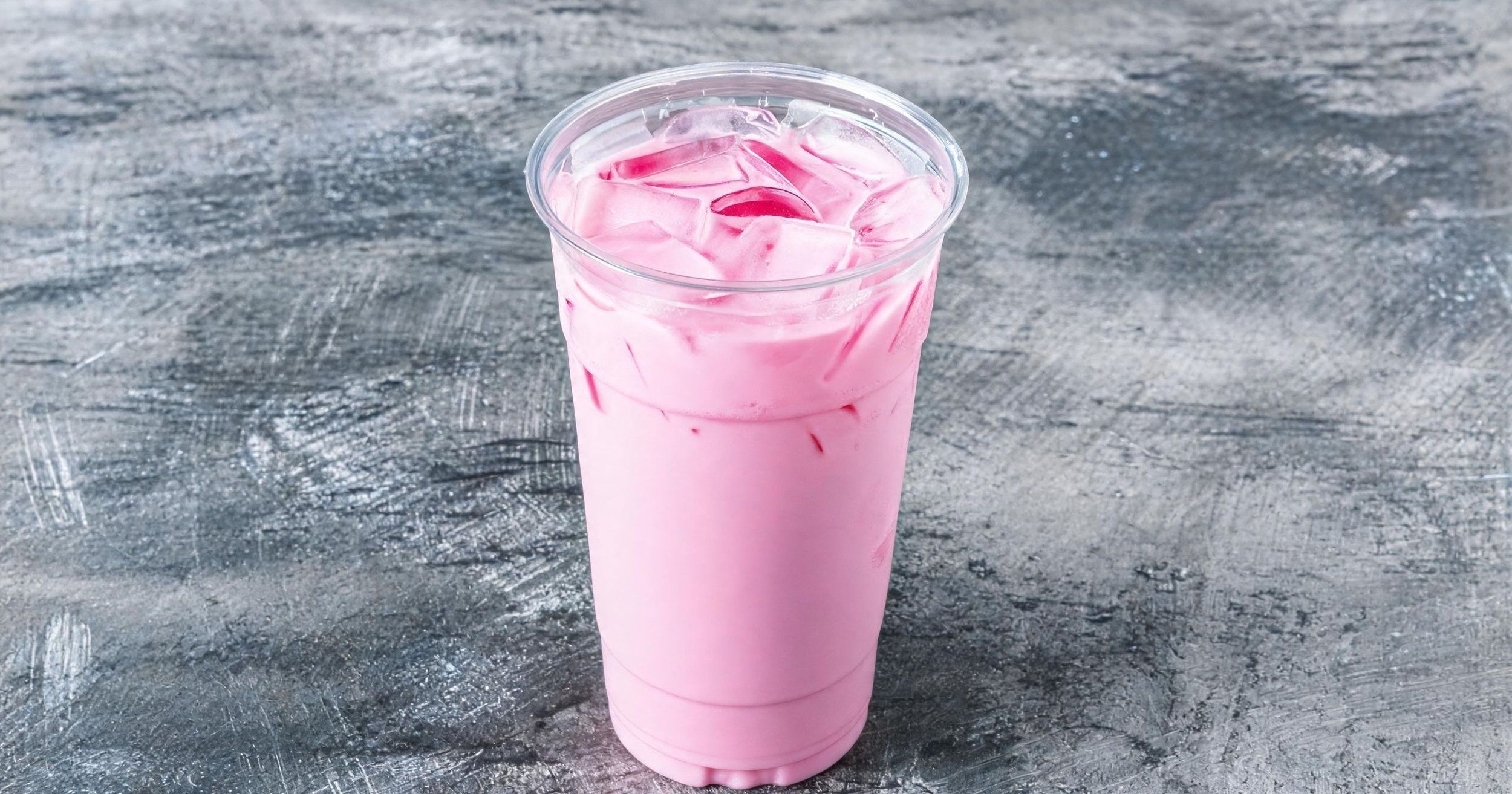 A clear plastic cup filled with pink iced beverage with swirls of darker pink and visible ice cubes, placed on a textured gray surface.