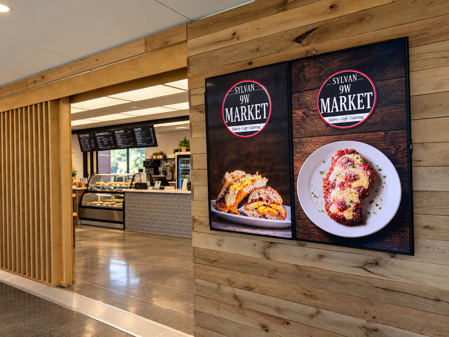 Two digital menu boards advertising food at Sylvan 9W Market, an eatery, cafe, and catering service, with images of dishes on a wooden wall near the cafe counter.