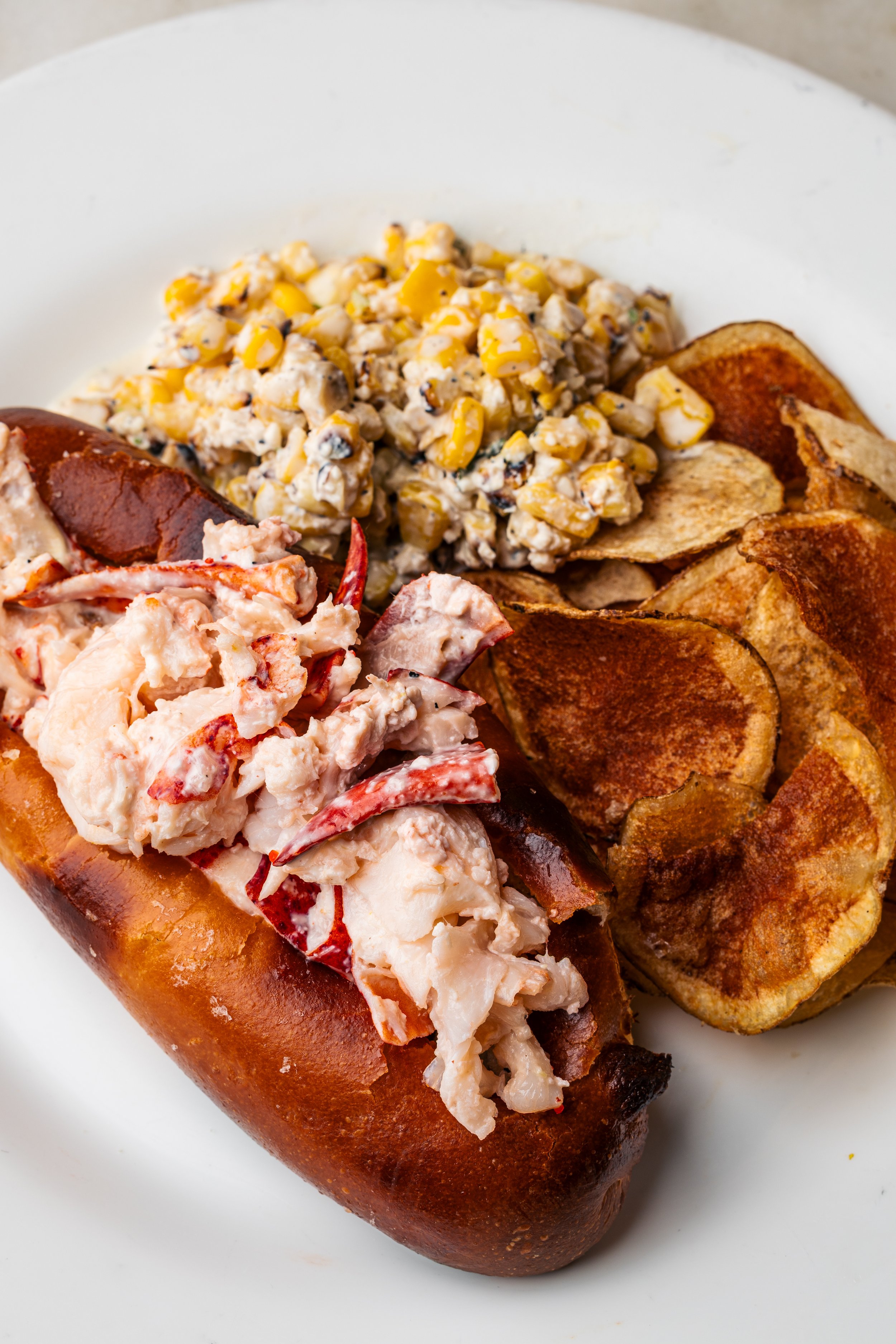 Lobster roll and potato chips on a white plate.