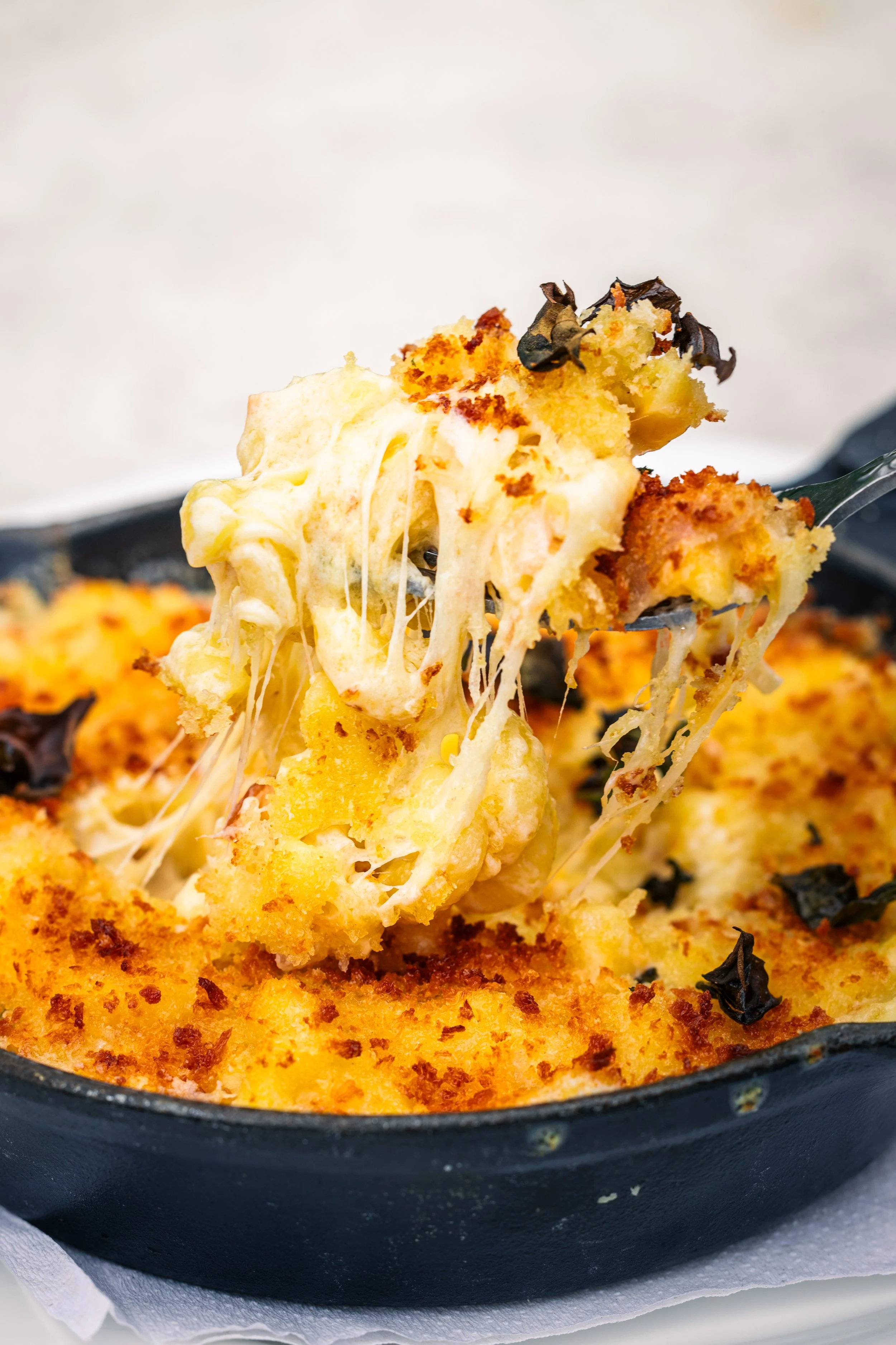 Close-up of a baked cheesy casserole in a cast iron skillet with melted cheese, breadcrumbs, and herbs.