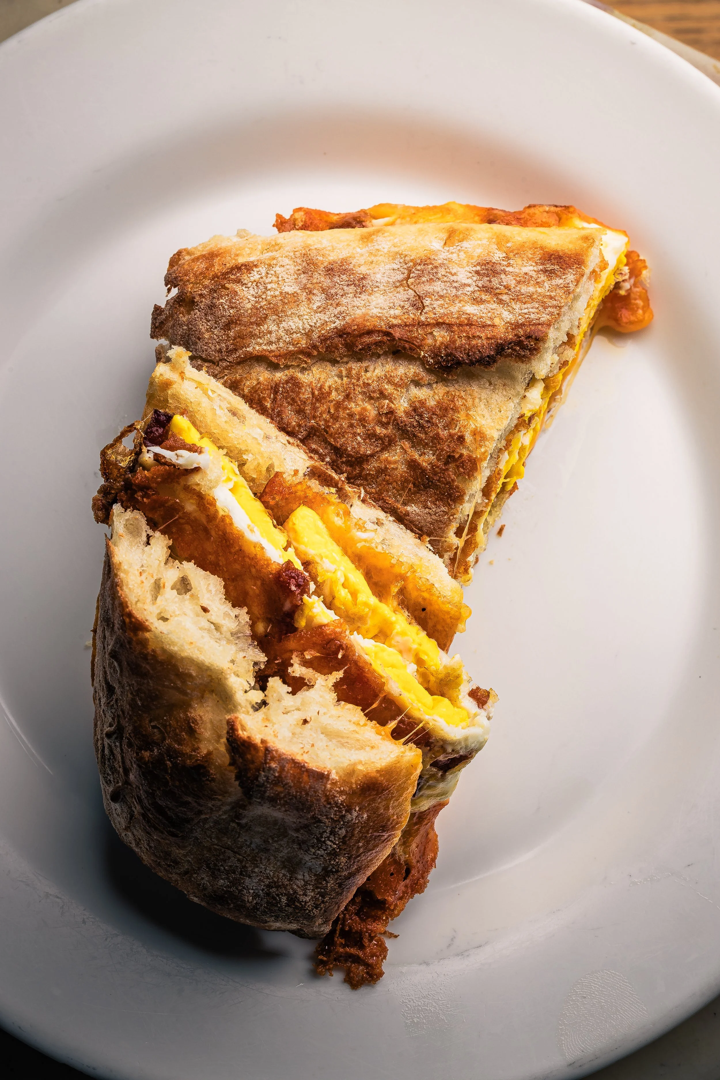 A slice of breakfast burrito with eggs, cheese, and meat in a toasted tortilla on a white plate.