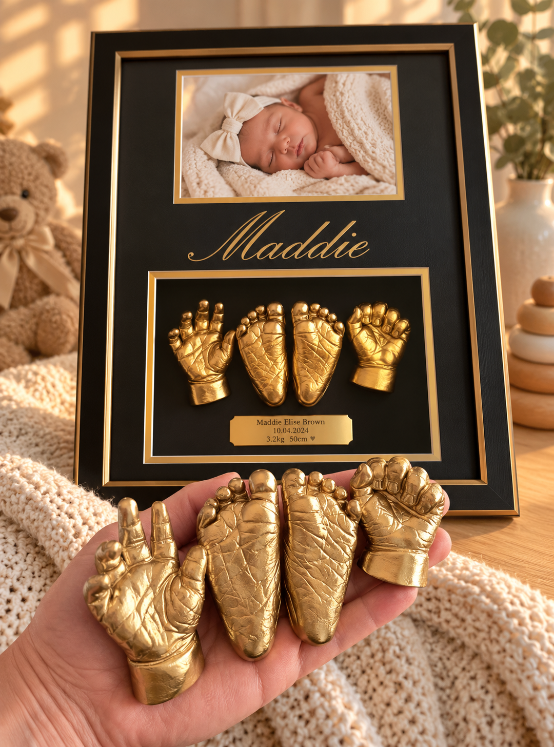 A framed photo of a sleeping baby girl with a bow, beside decorative golden baby hand and foot impressions labeled with name Maddie, birth date, weight, and length. Someone holds matching golden hand and foot imprints in front of the frame.