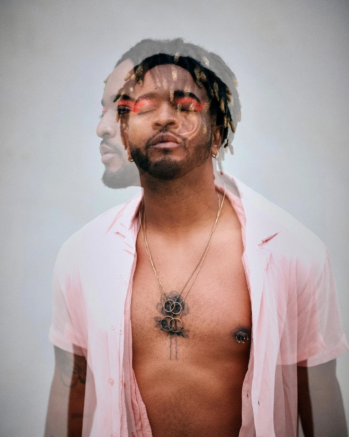 A person with multiple tattoos, jewelry, and piercings wearing an open pink shirt, with a layered artistic photograph effect showing both front and side views.
