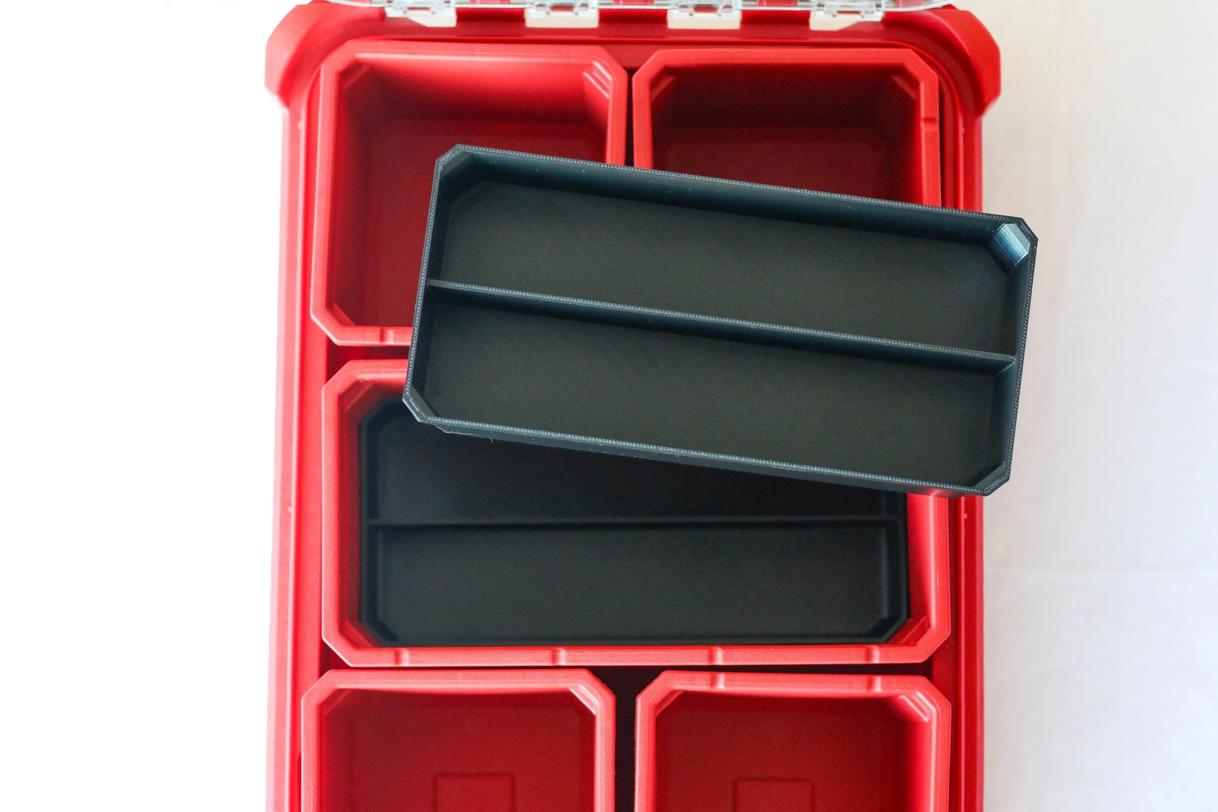 Red plastic storage container with multiple compartments, containing black plastic trays.