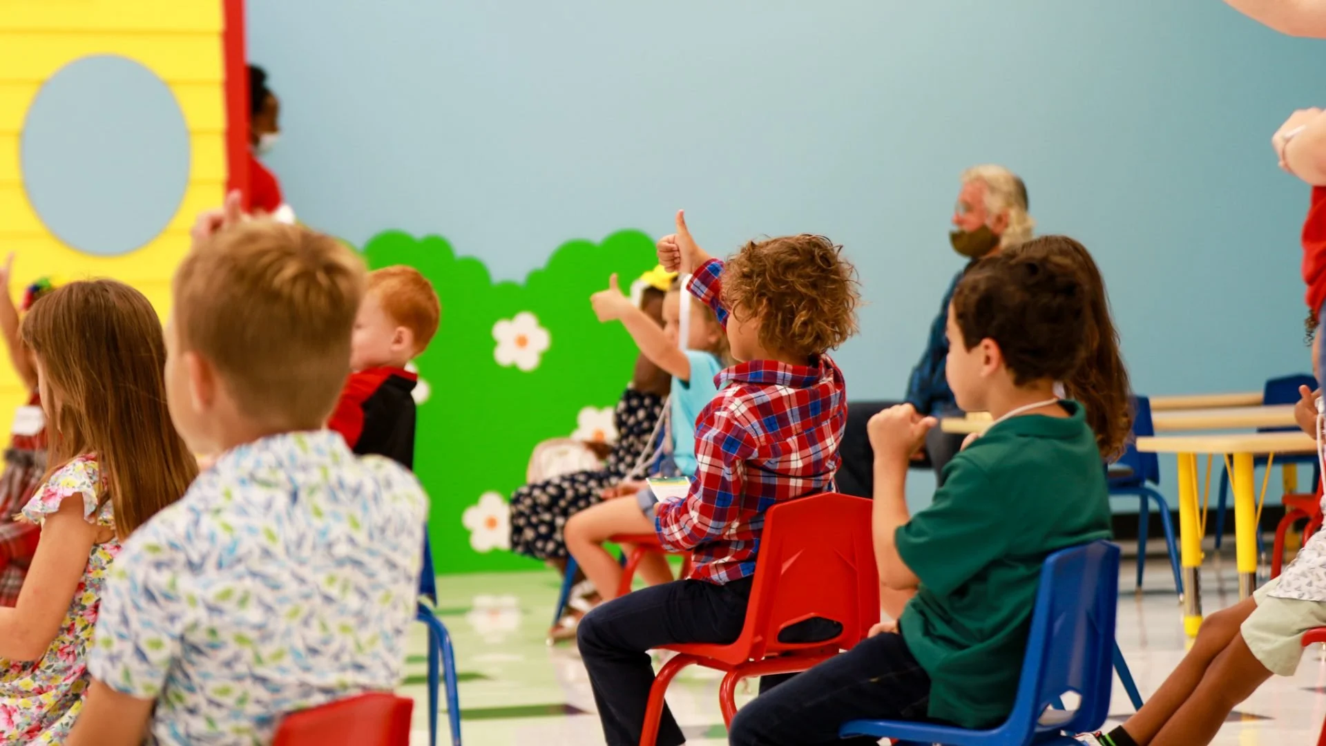 Toddlers sitting in a circle raising their hands.