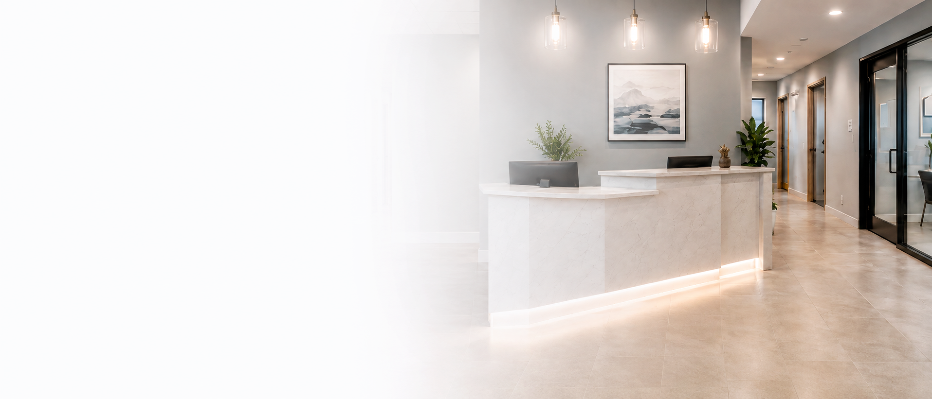 Modern reception area with a white curved marble desk, potted plants, framed artwork on light gray wall, pendant lights, and hallway with glass door and wooden framed doors.