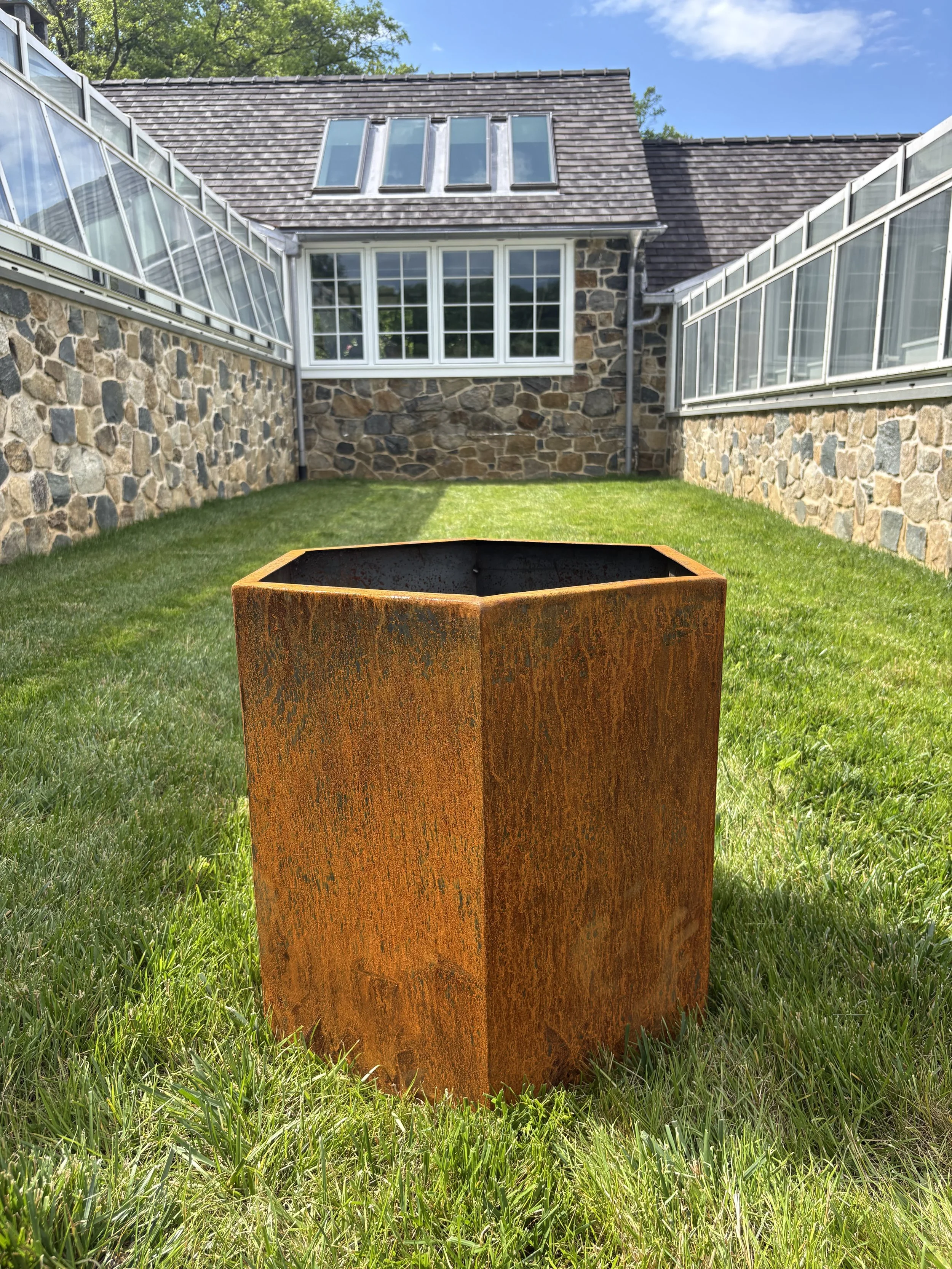 Corten hexagon planter sitting in front of a stone greenhouse in Greenville DE
