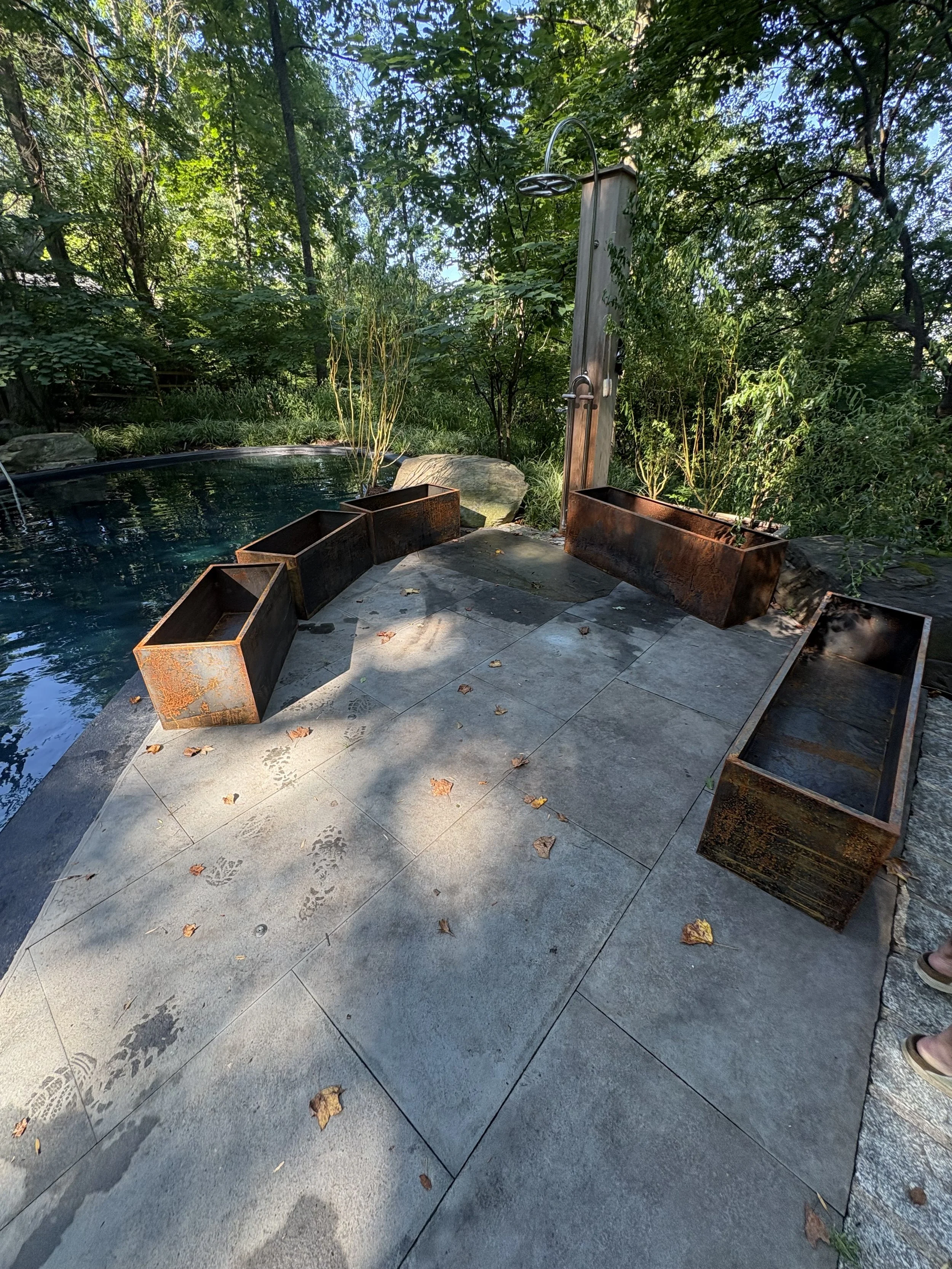 Outdoor shower area with Corten steel planters, a stone water basin, surrounded by lush greenery and shaded by trees in Glenside, philadelphia