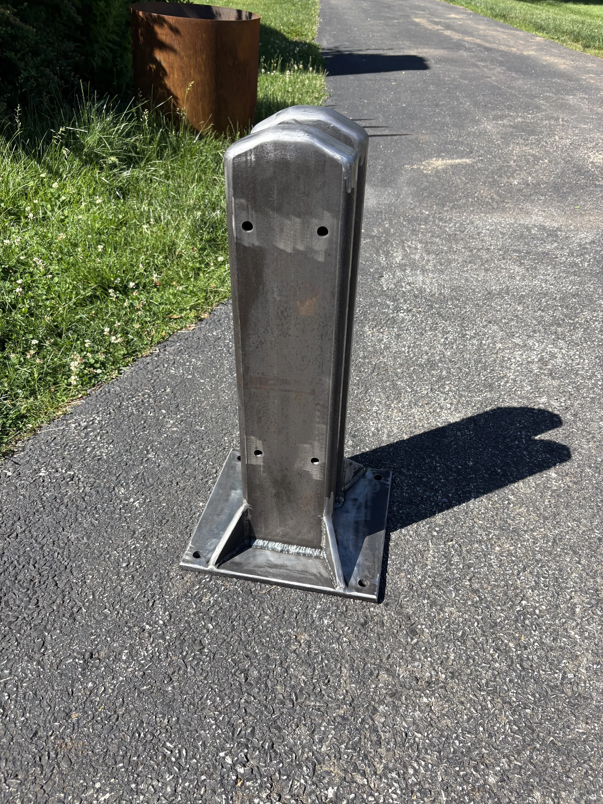 A metal flagpole on a paved asphalt surface with grass.