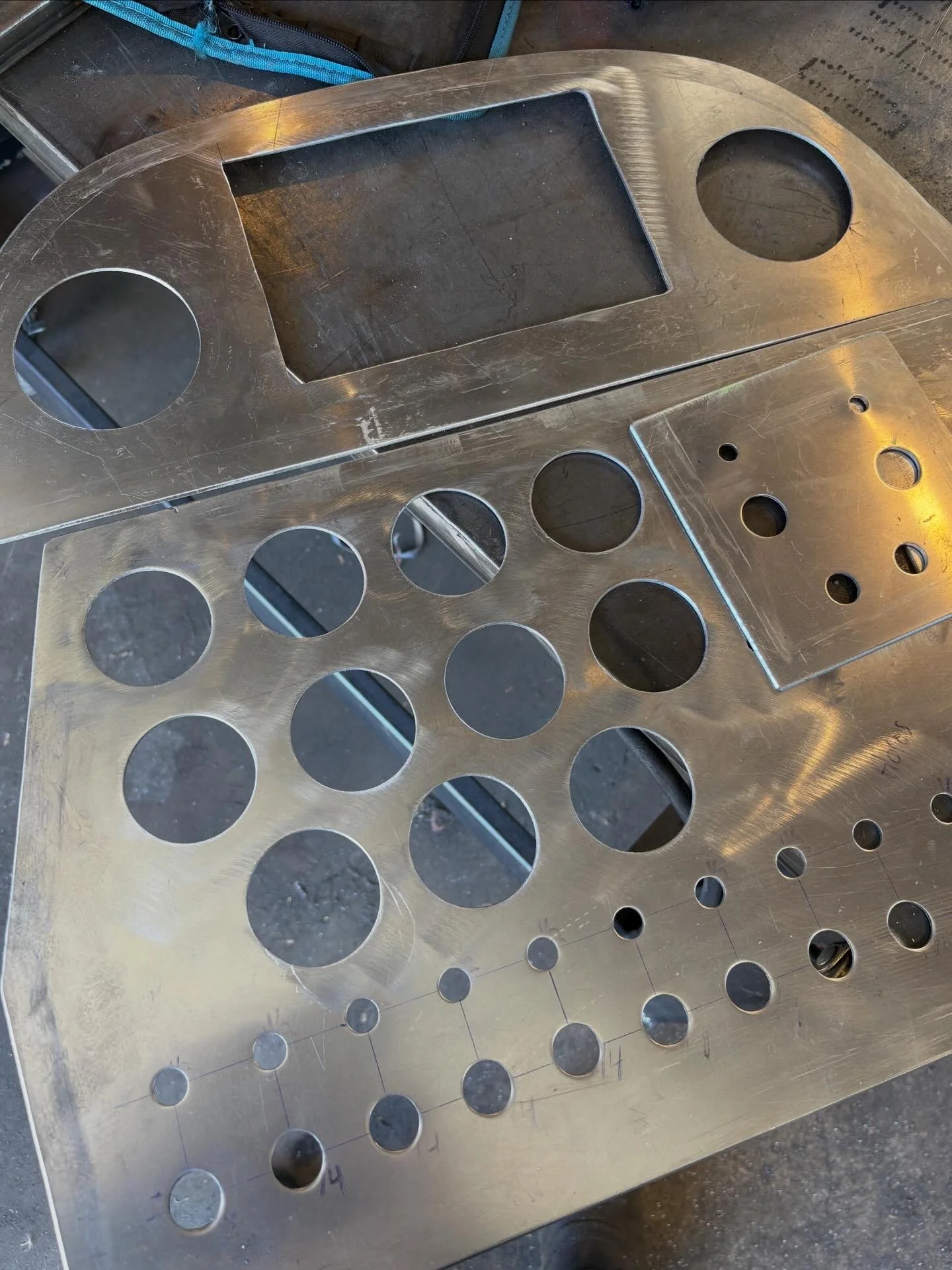 Two aluminum dash panels with multiple circular holes in various sizes on a worktable.