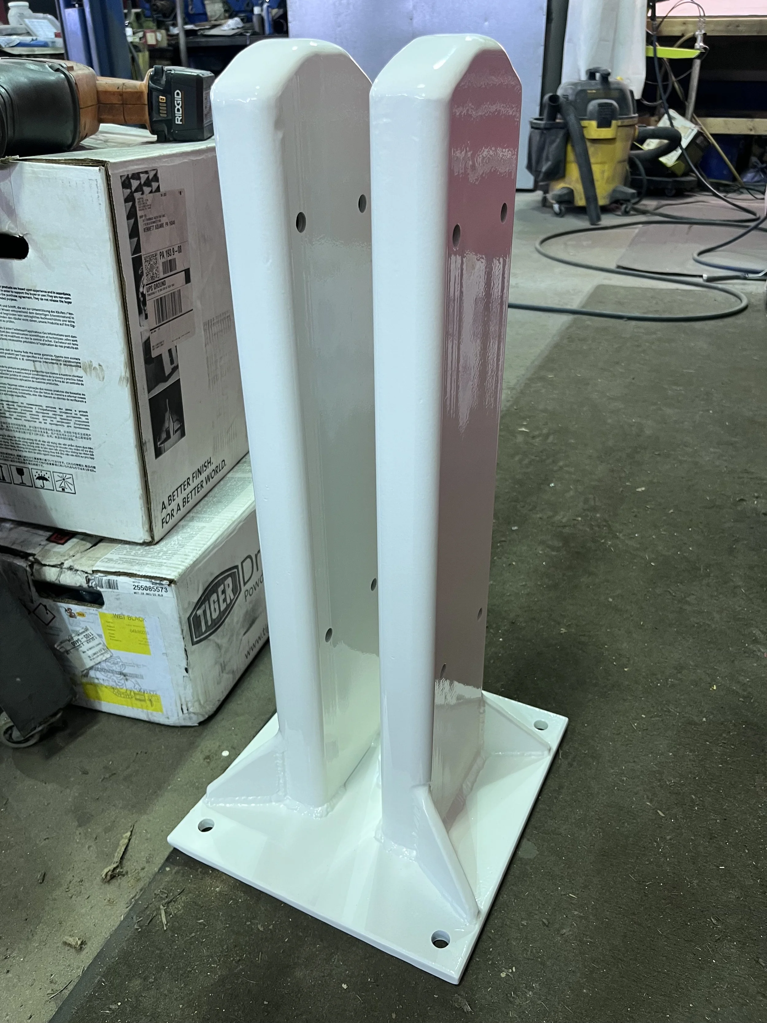 White metal stand with four vertical supports on a workshop floor surrounded by tools and boxes.