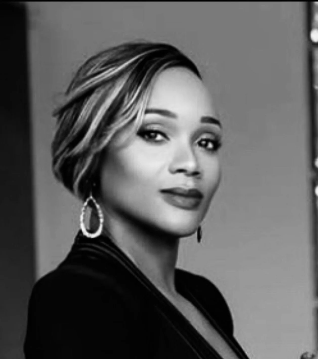 A black and white portrait of Faybiann Sutherland, wearing earrings and a dark top, looking at the camera.