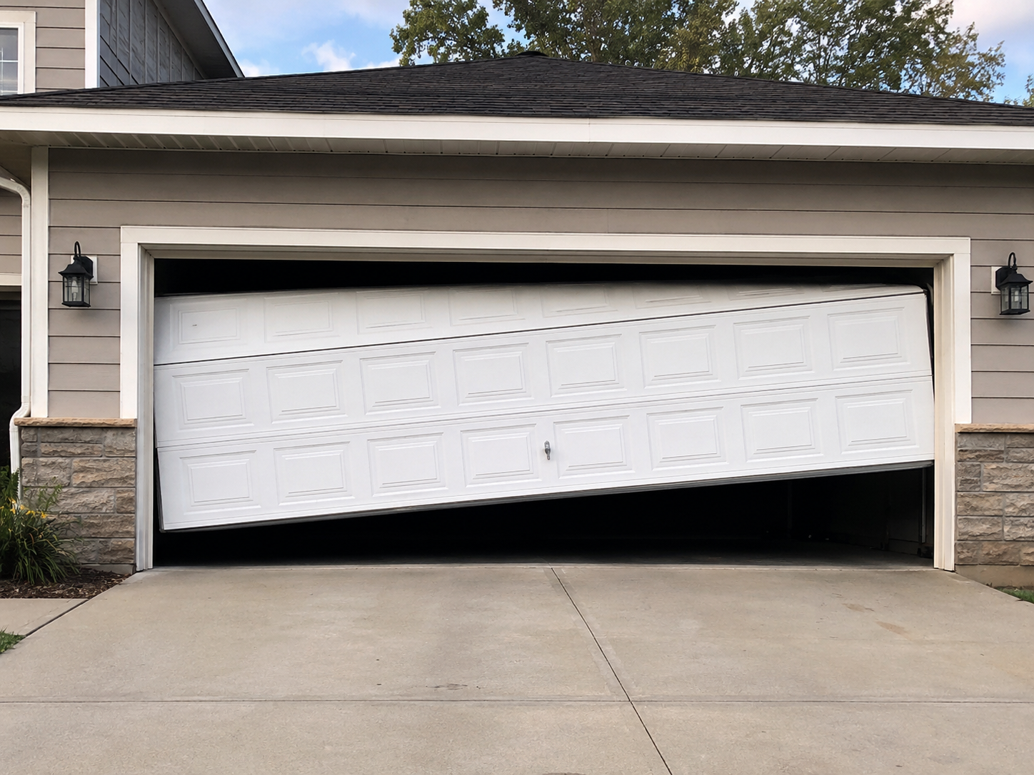 A white garage door that is partially open and leaning at an angle inside the garage opening of a beige house with stone accents. The garage is on a concrete driveway, and there are two black outdoor lantern-style lights on either side of the garage.