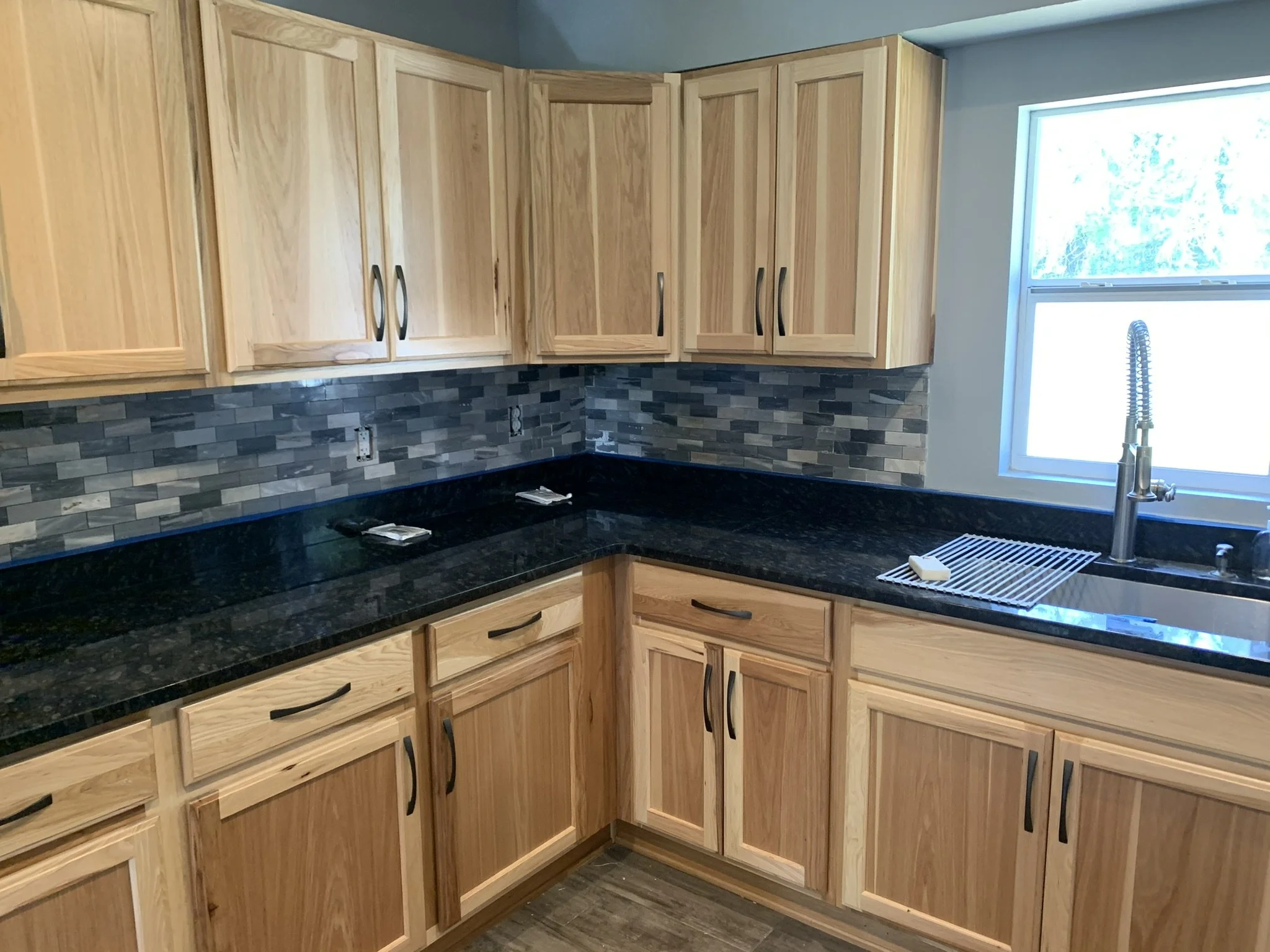 Kitchen remodeling and interior finish update with wood cabinetry, dark countertops, and tile backsplash installed by HavenForged in Sarasota, Florida.