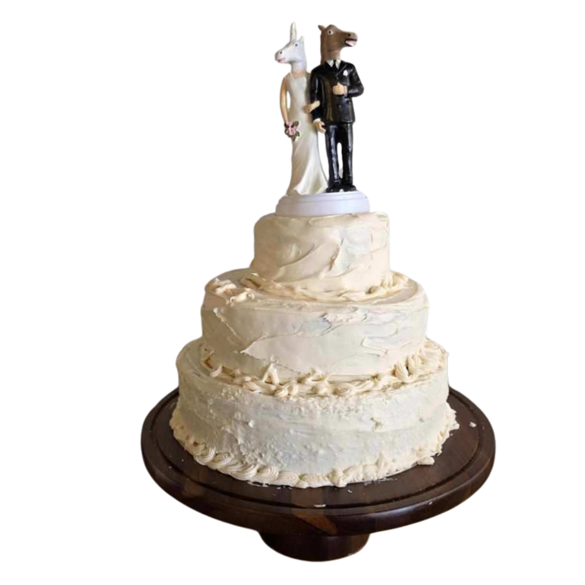 Cake with a wedding cake topper of a rabbit and a horse dressed as a bride and groom, on a wooden cake stand.