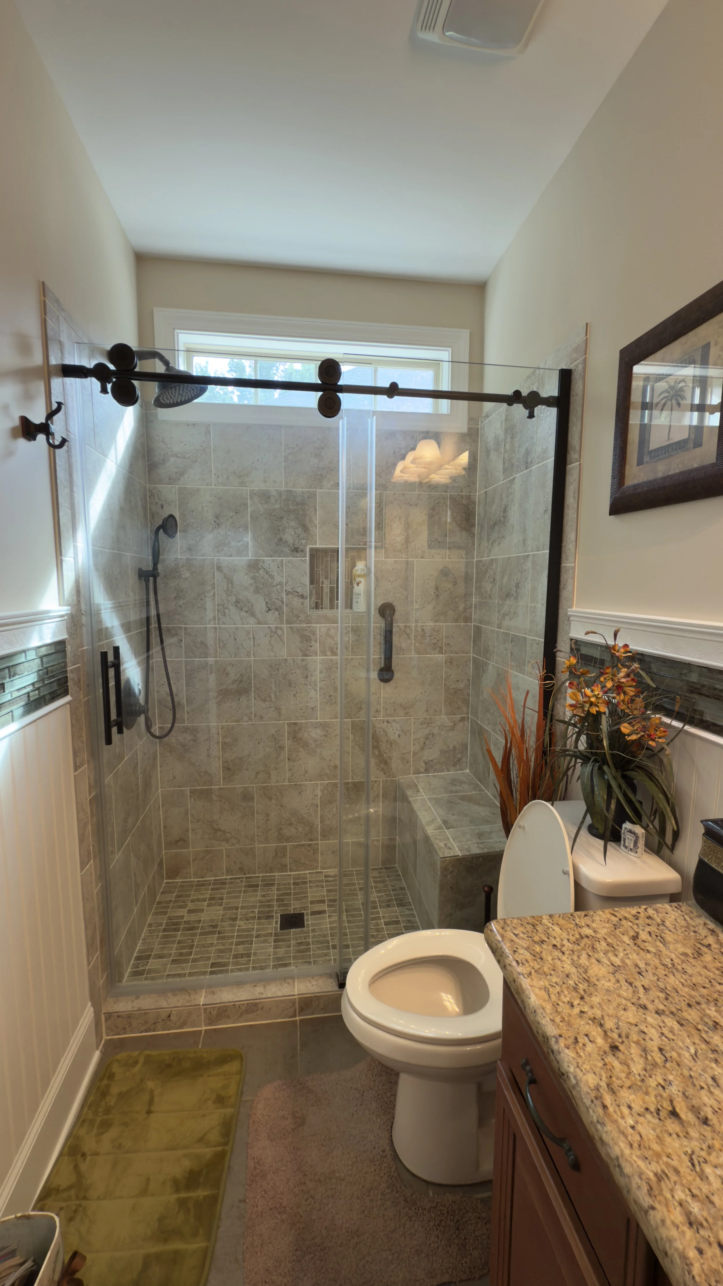 Bathroom with walk-in shower, toilet, and vanity with granite countertop. Decor includes a potted plant and framed picture on the wall.