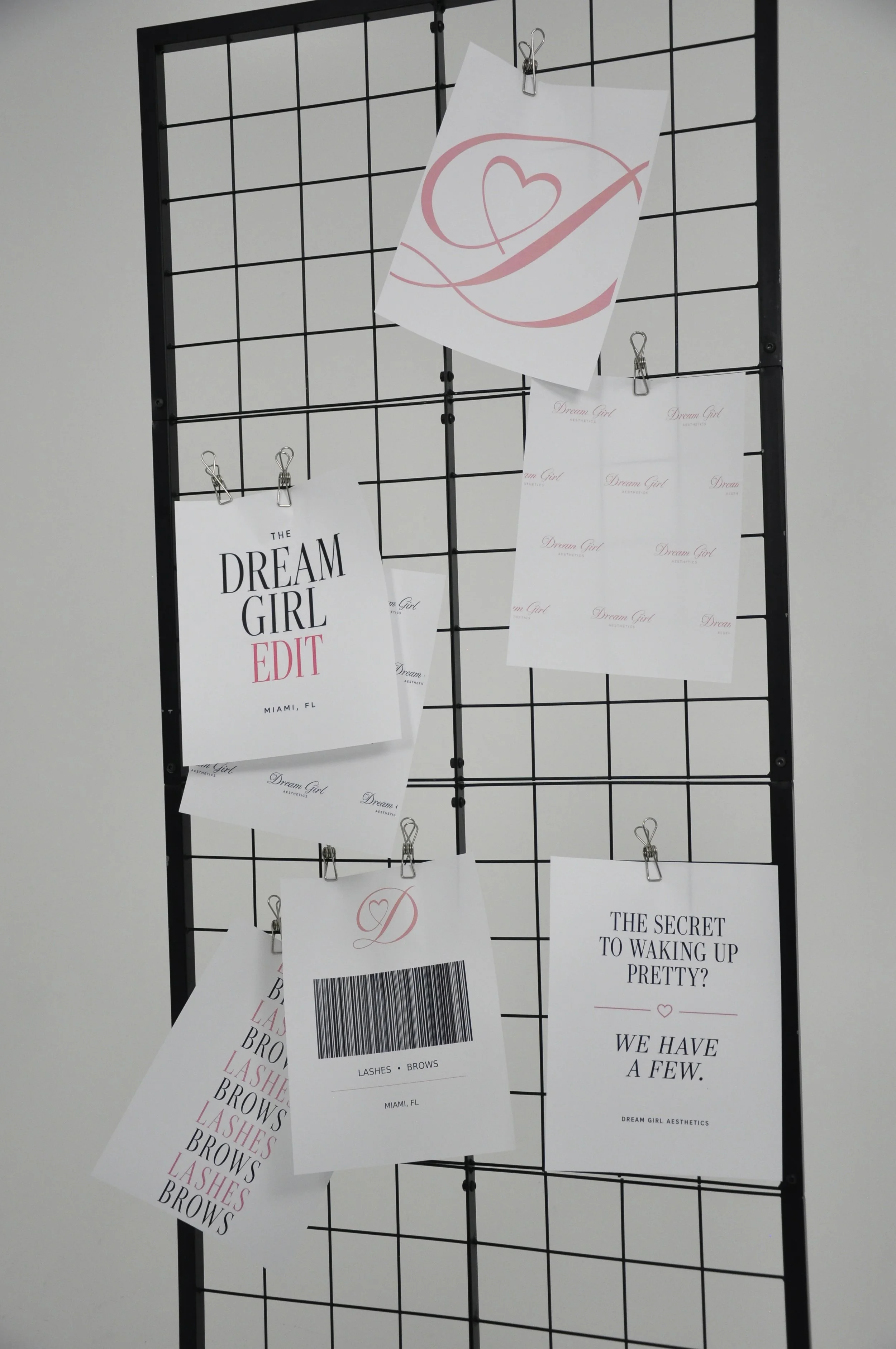 A black grid display board with multiple printed papers attached with clips, some showing text about beauty services and quotes. One paper has a pink drawn heart with a check mark.