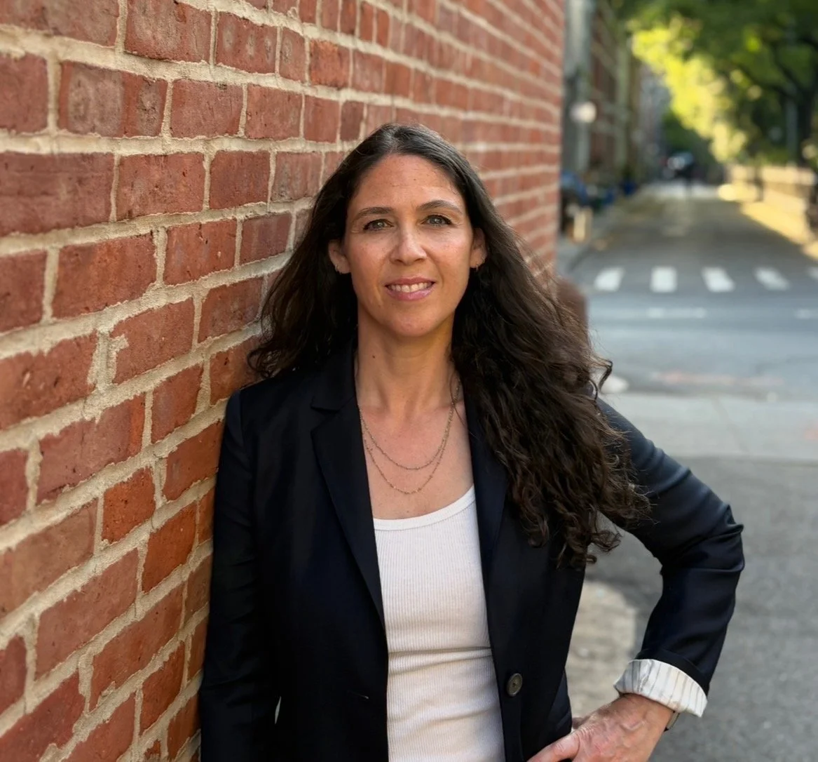 Dr. Eve Freidl, MD, standing outside against a brick wall on a tree-lined city street.