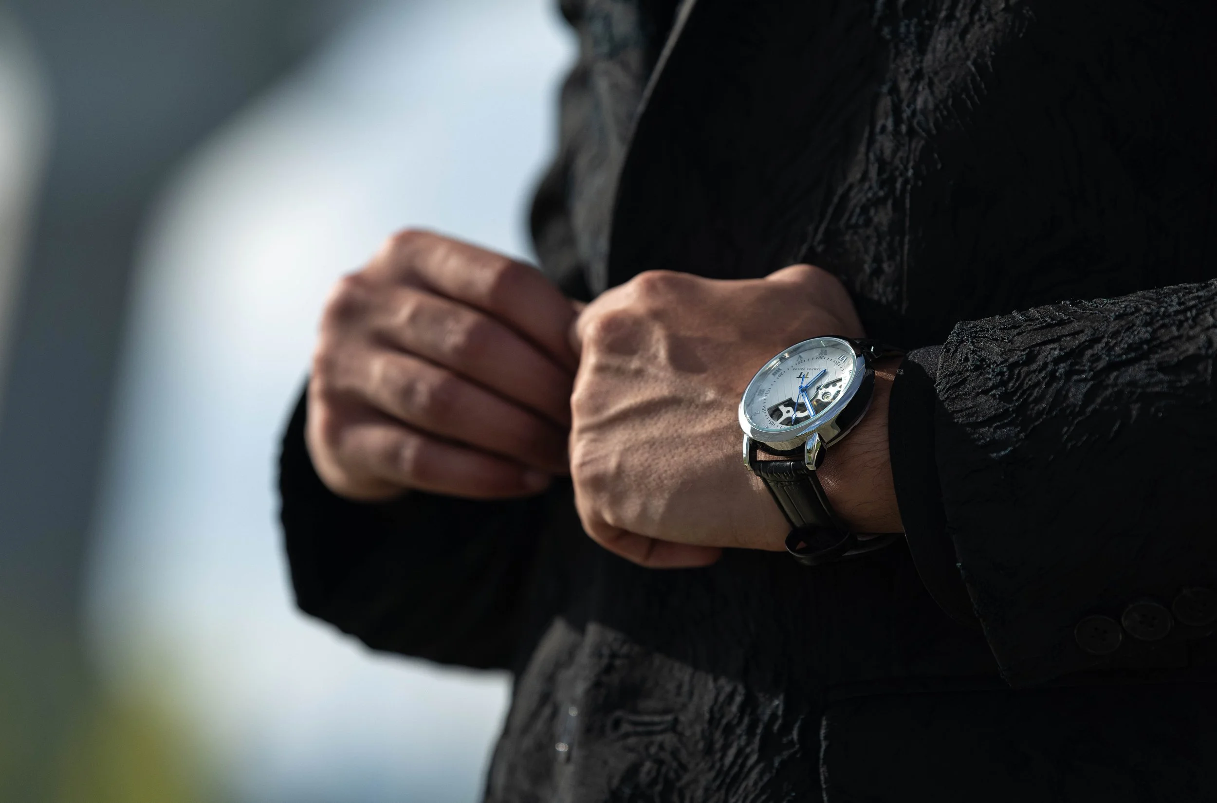 Close-up of a person adjusting their wristwatch while sitting on a textured surface outdoors.
