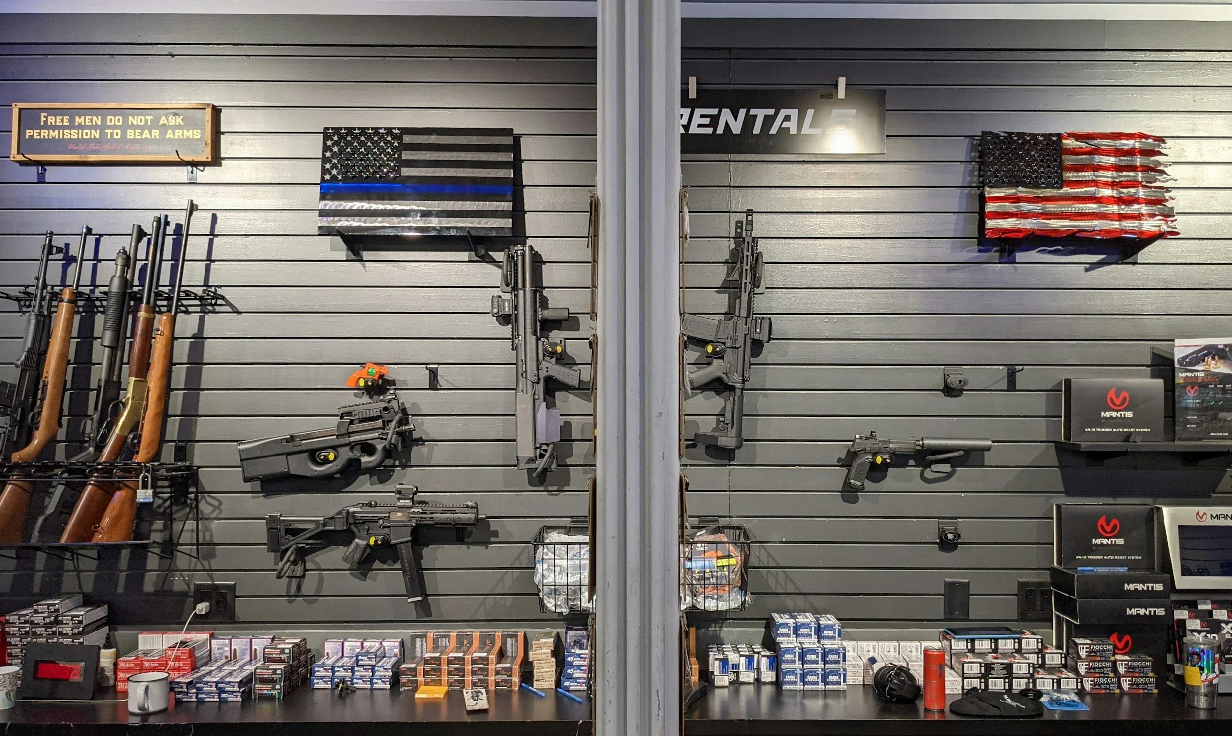 Display of firearms and ammo on a store wall, including guns, rifles, magazines, and ammunition boxes, with signage and fittings.