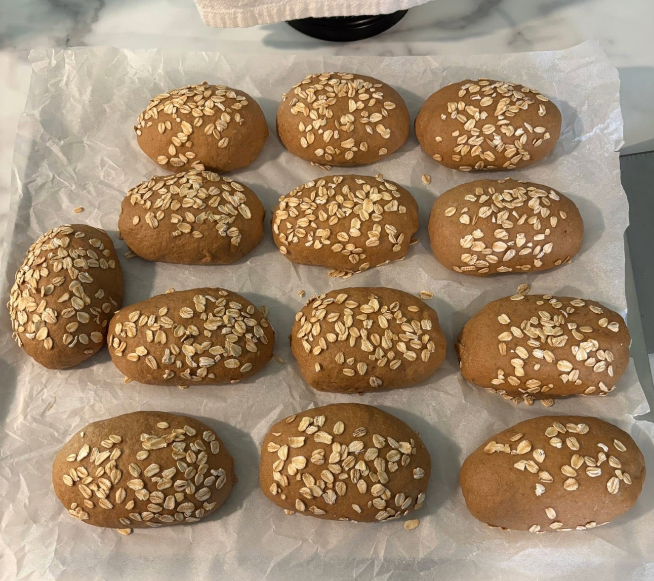 Fresh-milled flour Cheesecake Factory-style brown bread rolls topped with oats on parchment paper.