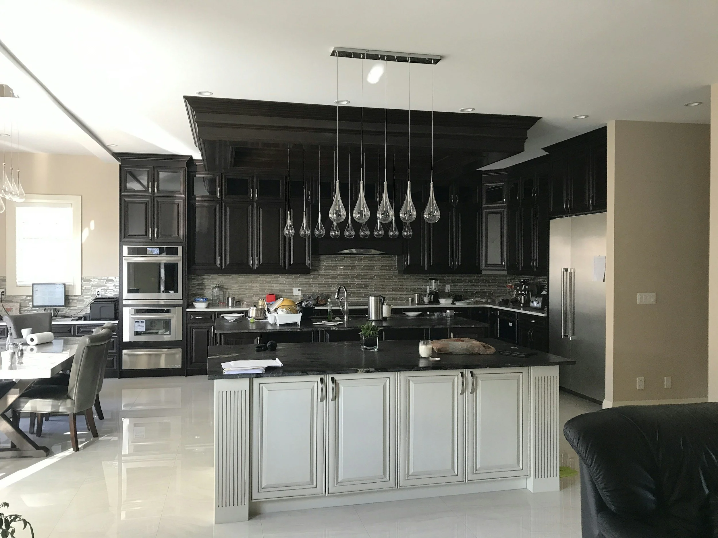 North Texas Home with modern kitchen with dark cabinets, a large central island, and a hanging chandelier with multiple teardrop glass fixtures.