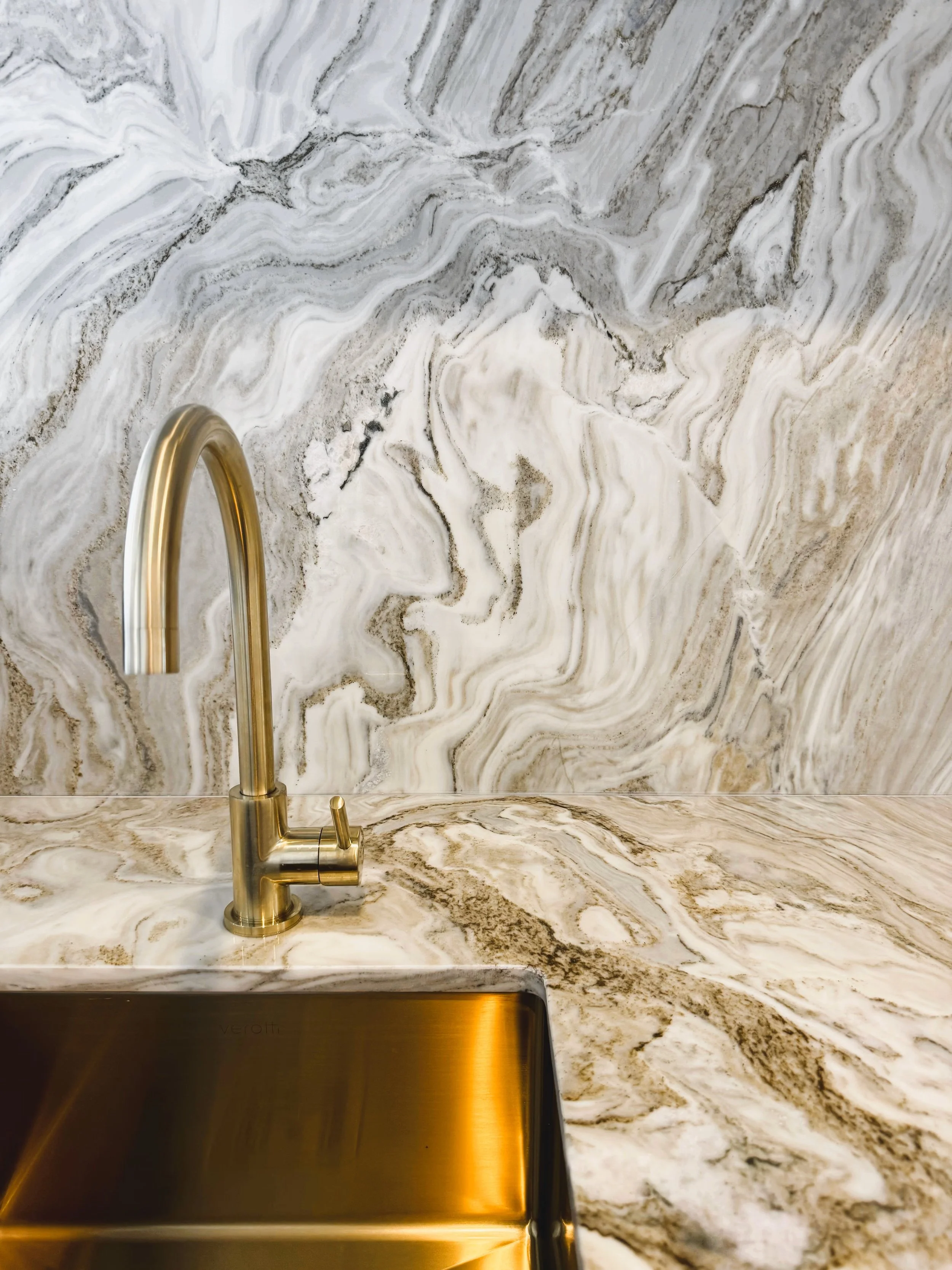 A kitchen countertop with a marble pattern and a stainless steel sink with a brass faucet.