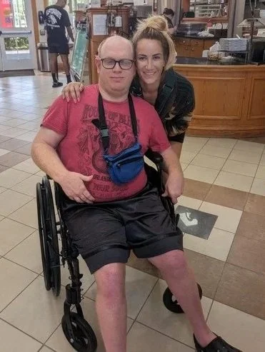Caring Breakthroughs LLC team member poses with client in a wheelchair.