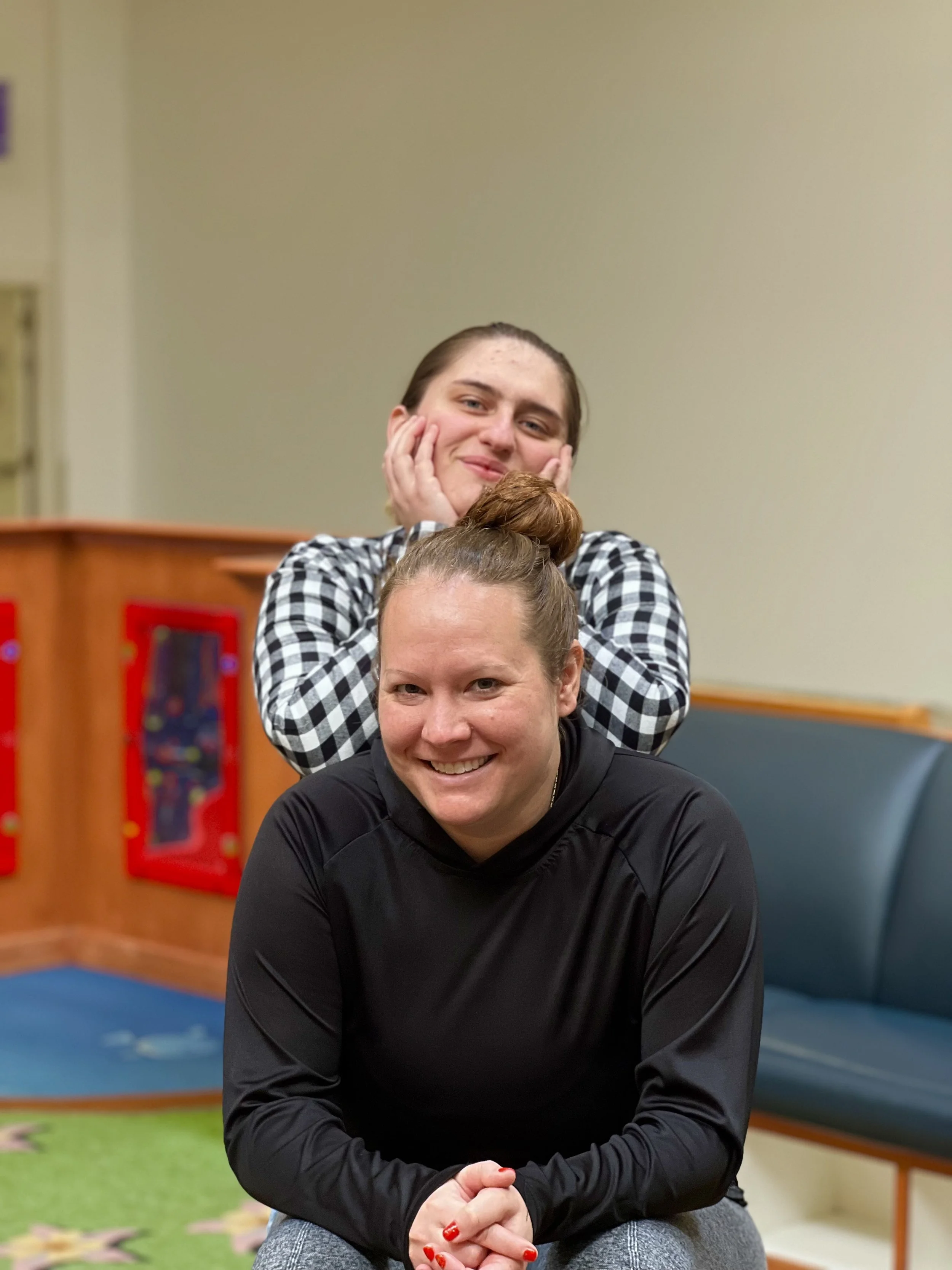 Grinning Breakthroughs LLC team member poses over the shoulder of a smiling fellow team member.