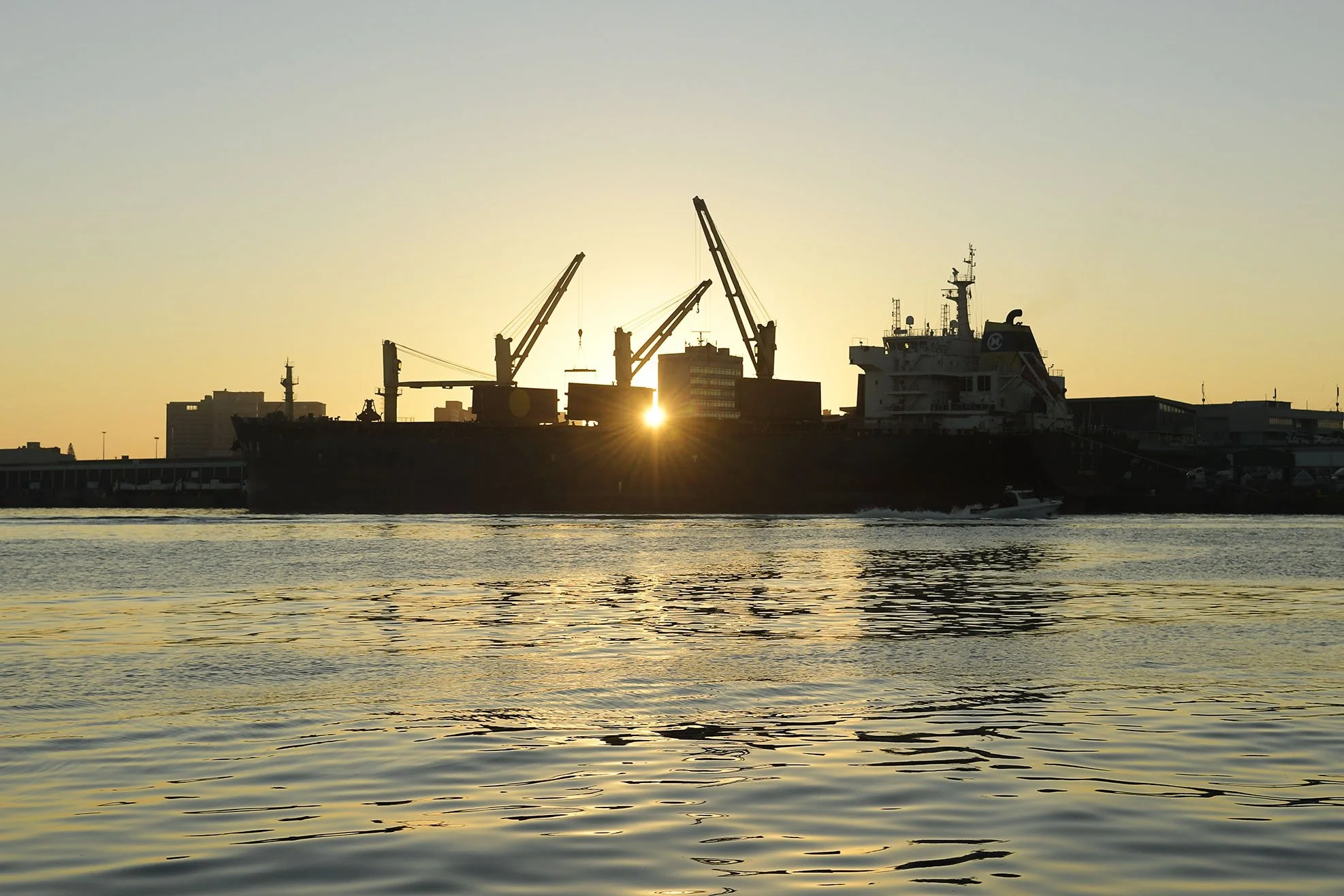 Background image of cargo ship silhouette at sunrise, turning the wheels of commerce in Durban