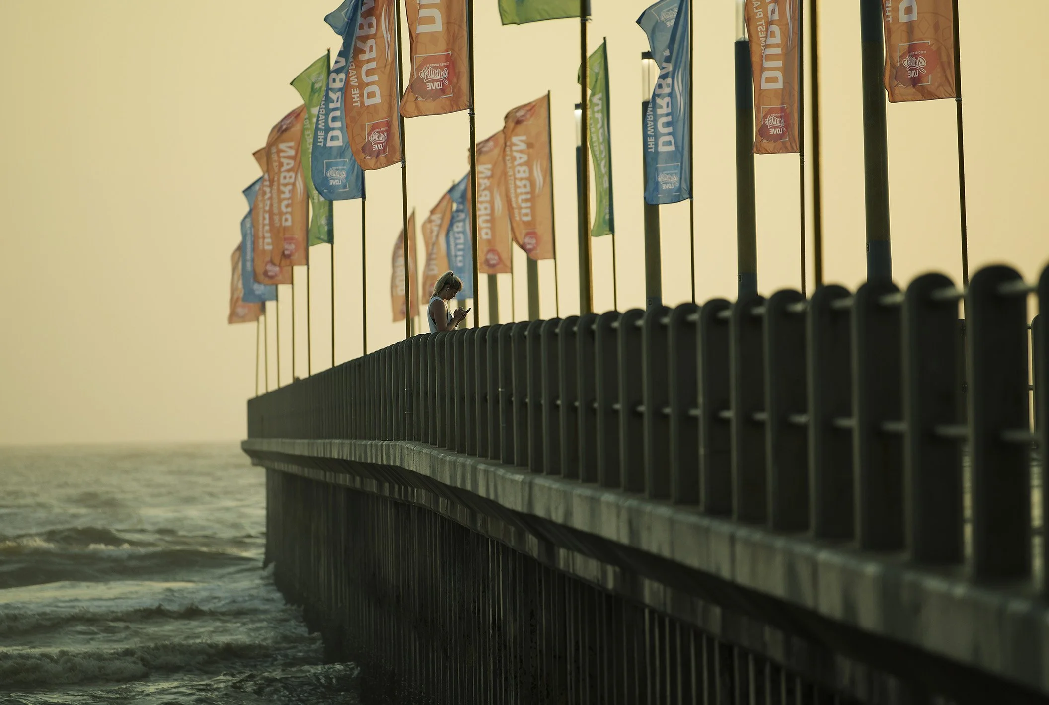 Mobile phone pause, woman standing on North Beach pier at daybreak
