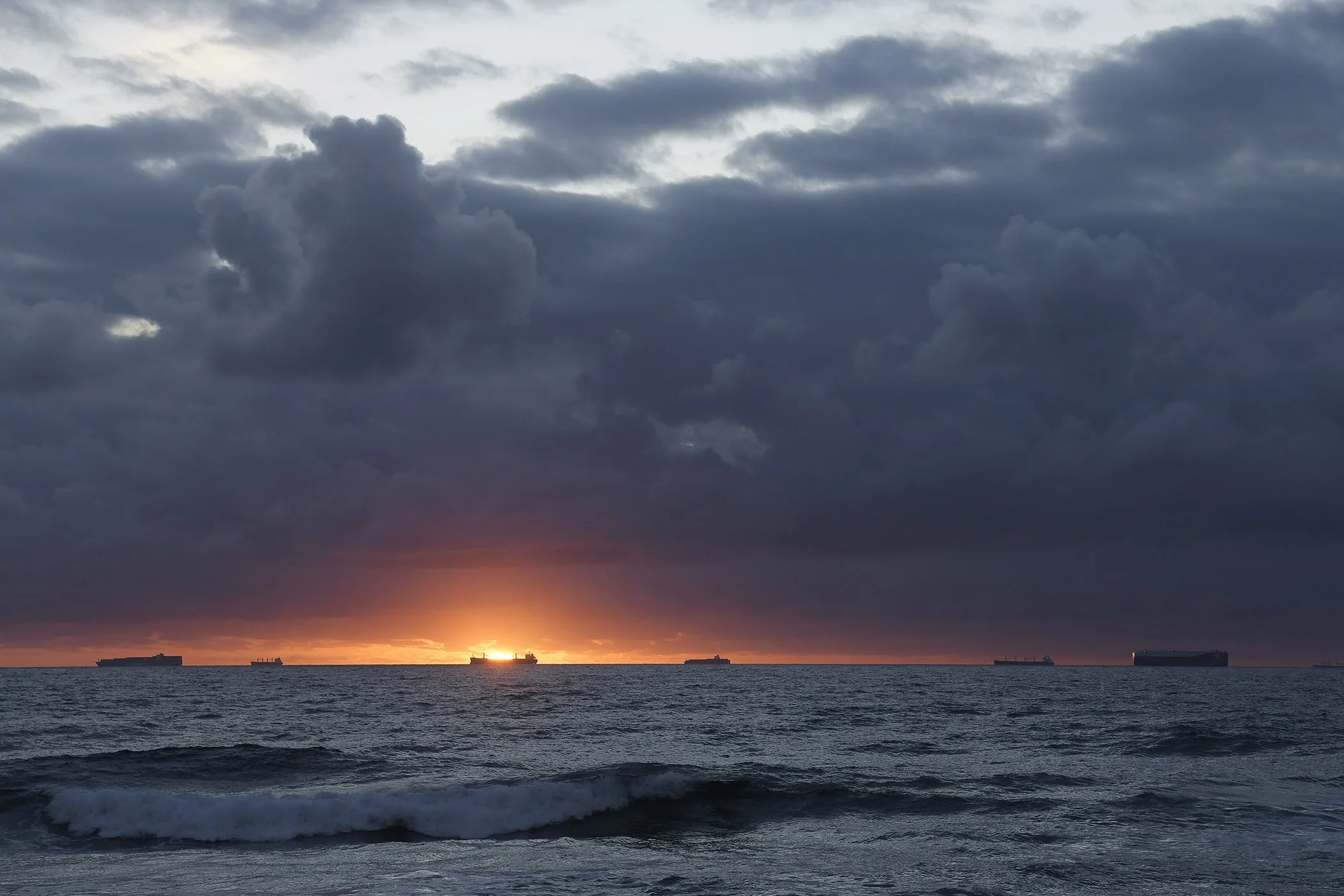 Mood photo of Indian Ocean at daybreak, cloudy dramatic sky and sun glowing orange on horizon 