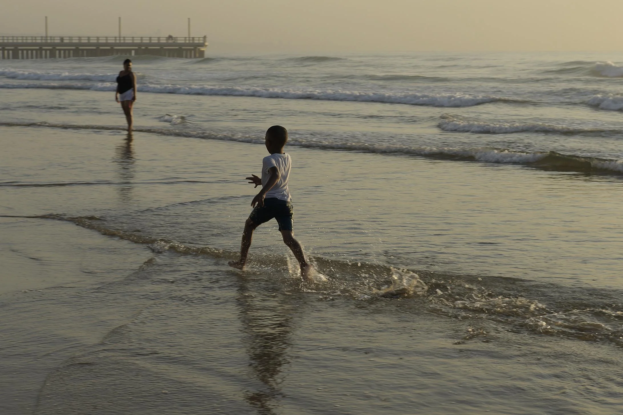 Early morning brings out joy, energetic young boy running in surf backwash