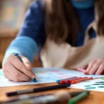 A person drawing with colored markers on paper, sitting at a wooden table.