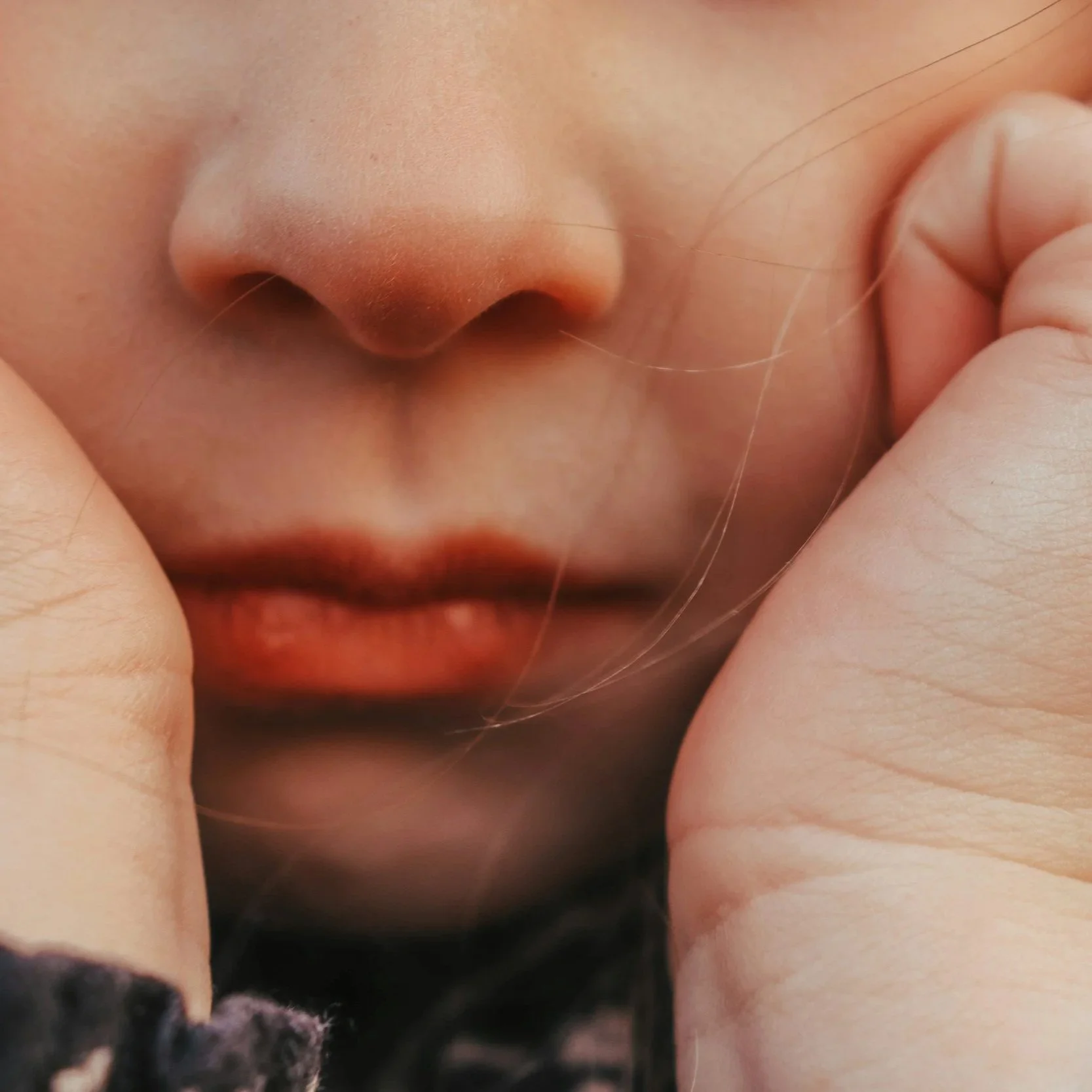 Close-up of a quiet child's closed mouth, with fingers gently holding the face.