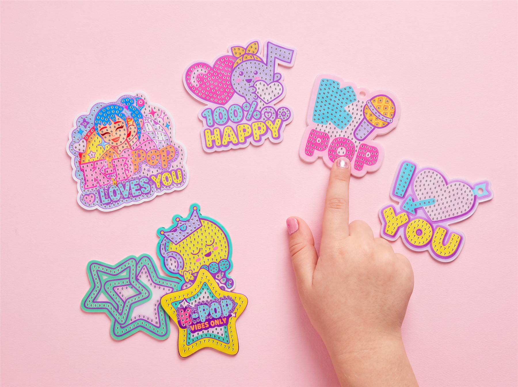 Sparkling gem stickers shaped like stars and badges on a pink table, with a hand pressing one