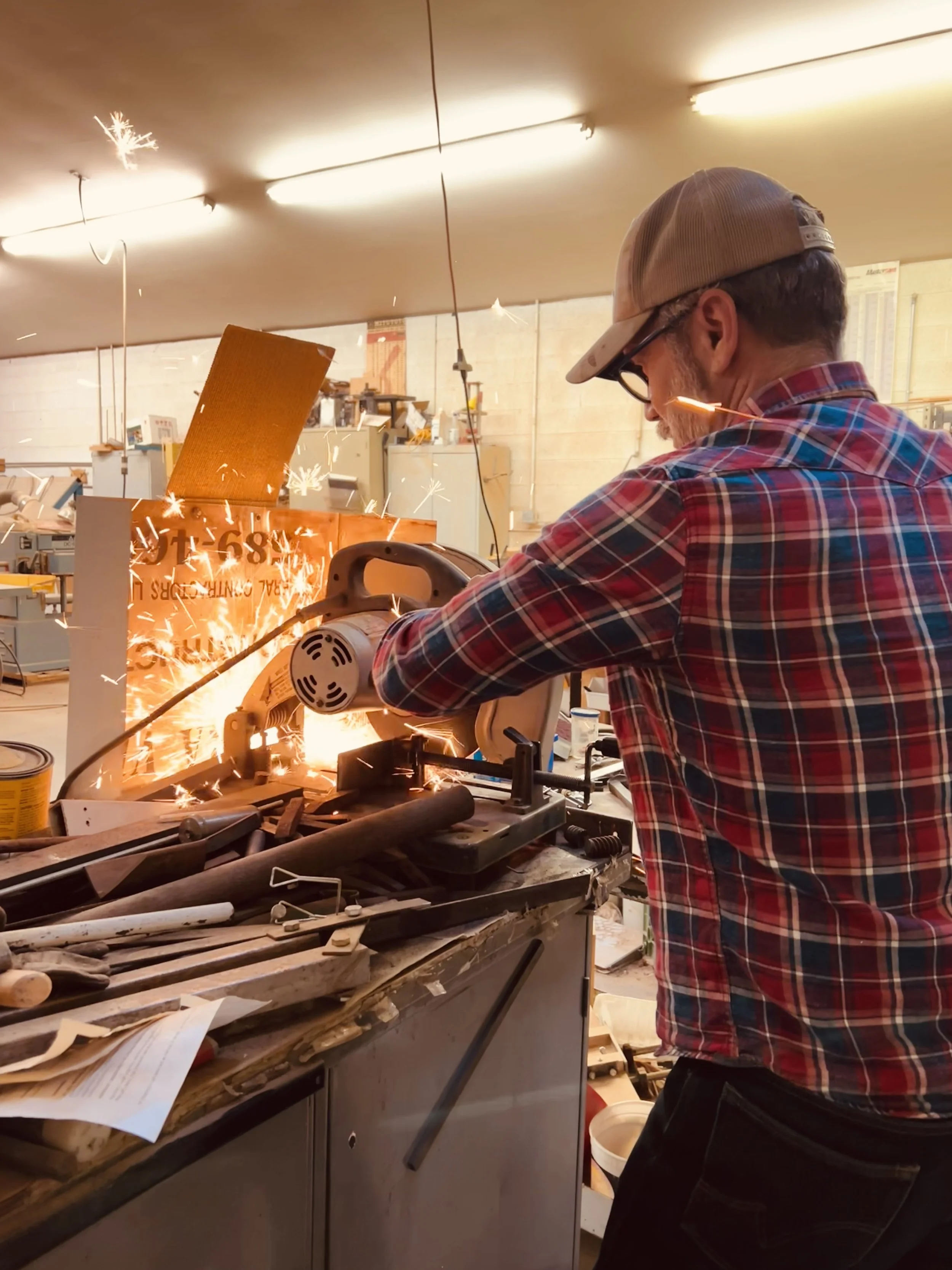 Ron Cole in Under The Pines Designs woodworking shop cutting railroad spikes to make red oak, mahogany, cherry, gamble oak, walnut, live edge coat hooks with custom engraving using a chop saw, Williams Arizona