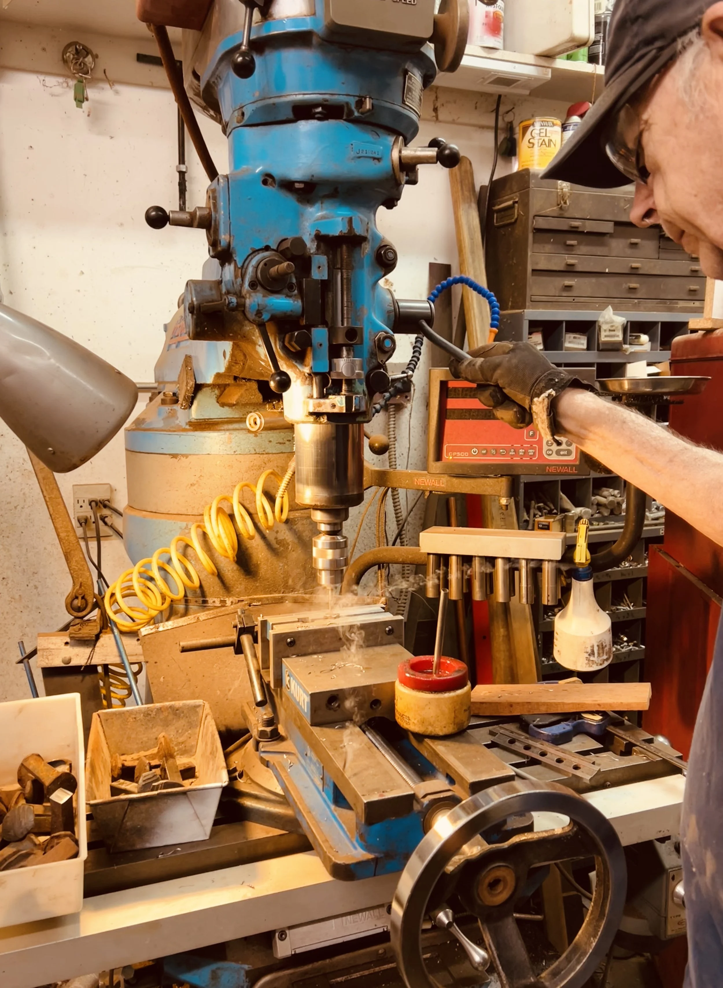 Don Nord at the Bridgeport industrial drill press mill tapping holes into the ends of cut railroad spikes to make custom coat hooks from live edge gambel oak, mahogany, cherry, walnut, and red oak in the wood shop of Under The Pines Designs, Williams