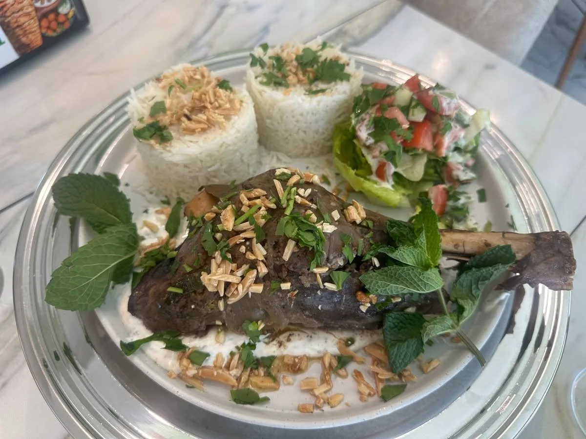 Plate with grilled lamb chop garnished with herbs, two cups of rice topped with herbs and nuts, and a small side salad with tomato, cucumber, and lettuce.