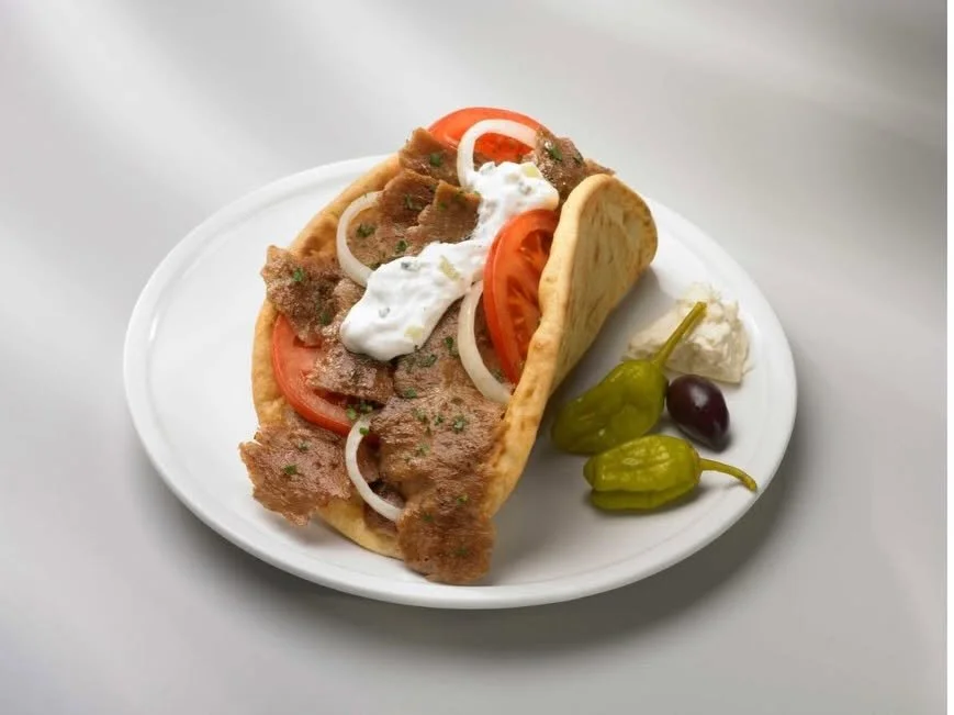 A plate with a taco filled with meat, tomato, onion, and sauce, served with green chili peppers, a black olive, and a dollop of sour cream.
