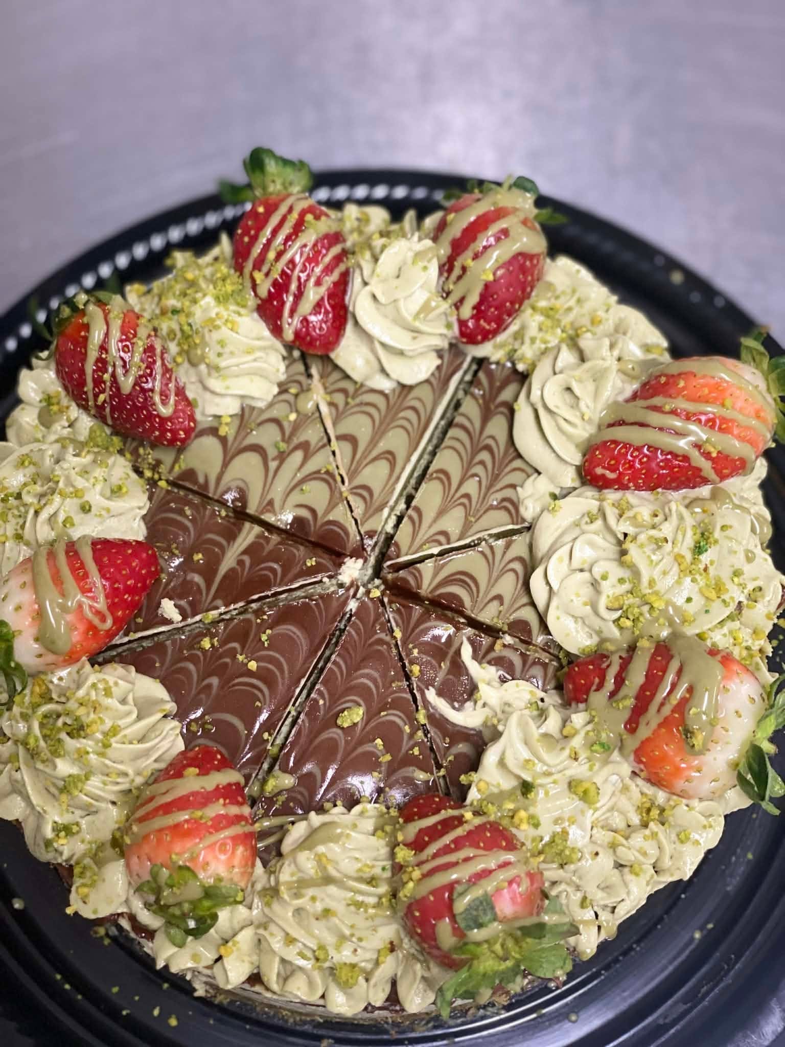 Chocolate and white marbled cake decorated with fresh strawberries, whipped cream, chopped pistachios, and drizzled with chocolate and white chocolate.