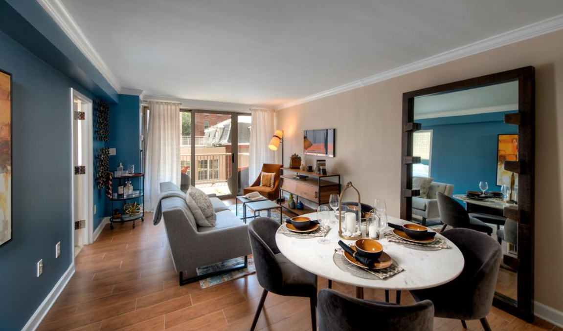 Living room with a dining area, sofa, armchair, wall-mounted TV, and sliding glass door leading to a balcony.