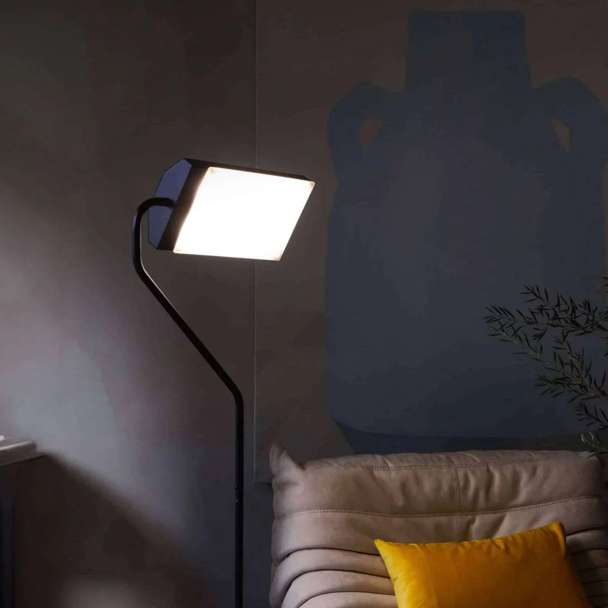 Modern floor lamp with a bright rectangular light, placed next to beige sofa with yellow pillow in a cozy living room.