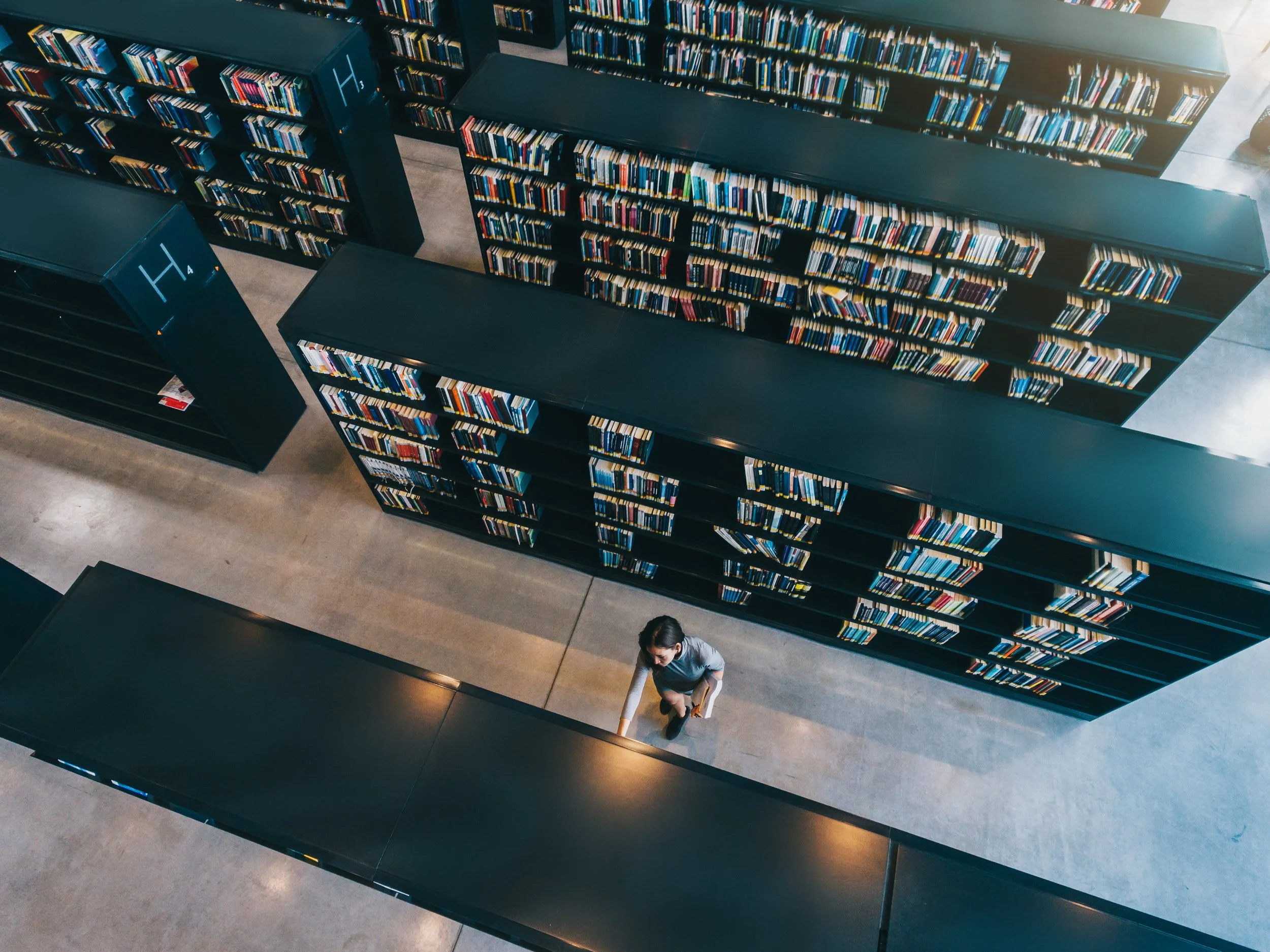 Person reading between tall library bookshelves