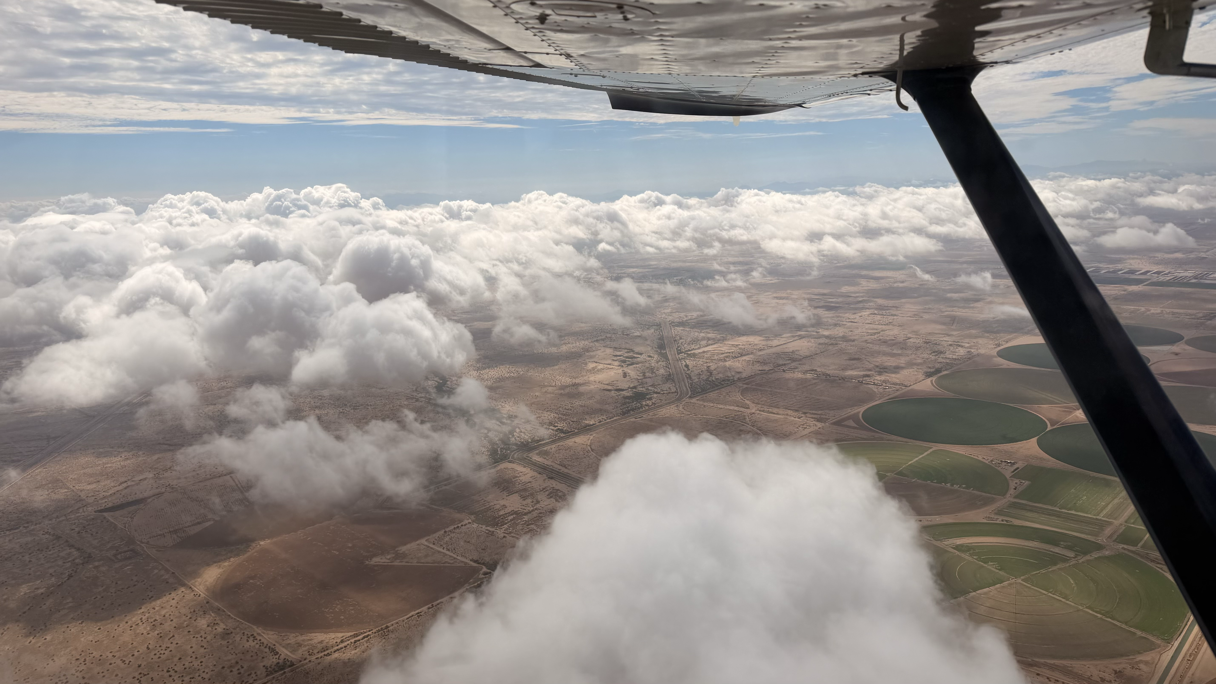View from a Wind Walker Cessna above clouds and farm fields.