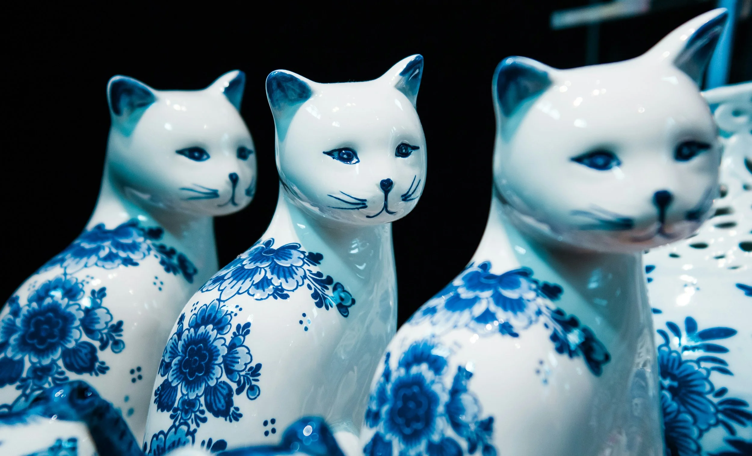 Collection of white porcelain cat figurines with blue floral designs, facing various directions, against a dark background.